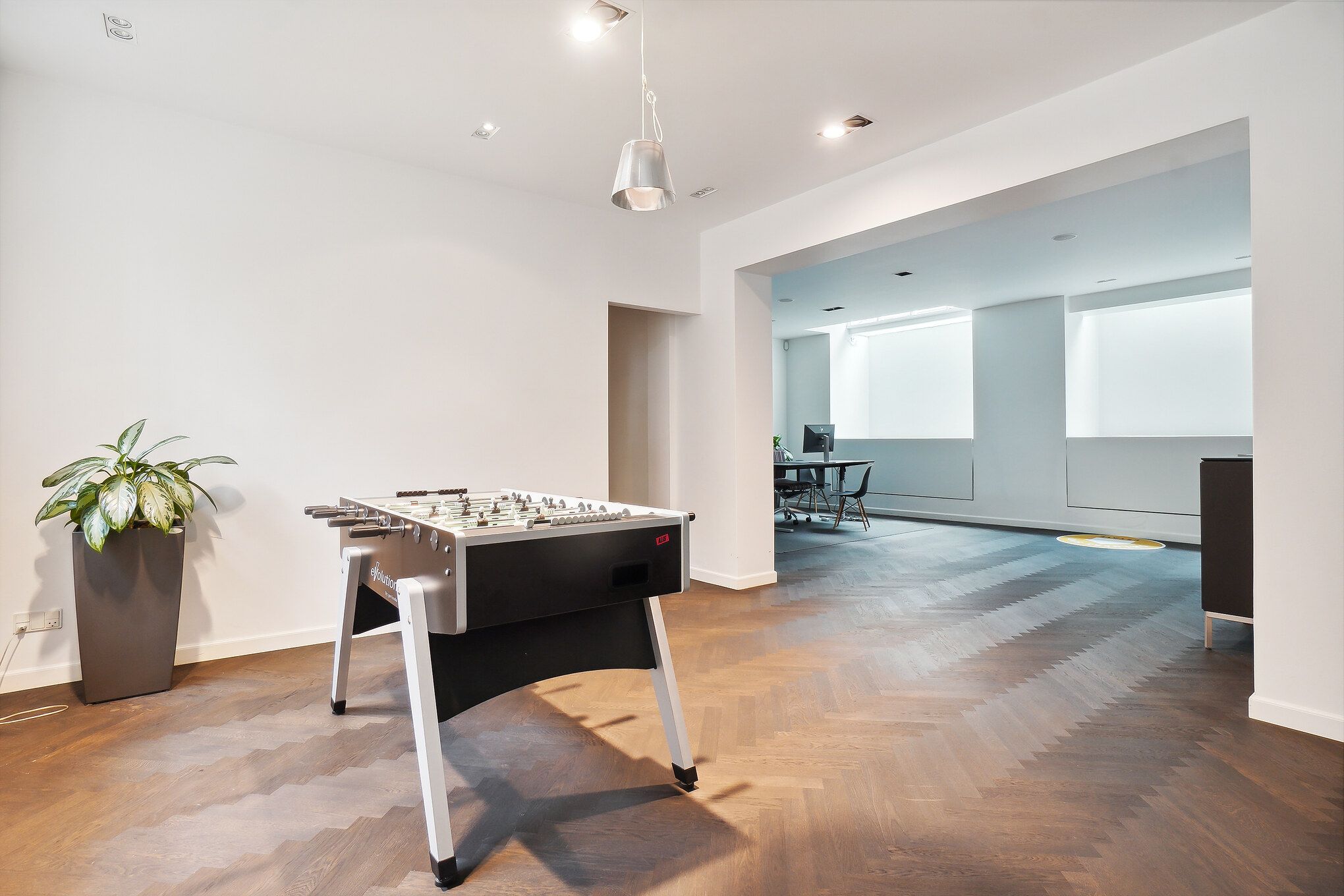 En minimalistisk stue med trægulve, en fodboldbord og en plante i en gryde i hjørnet