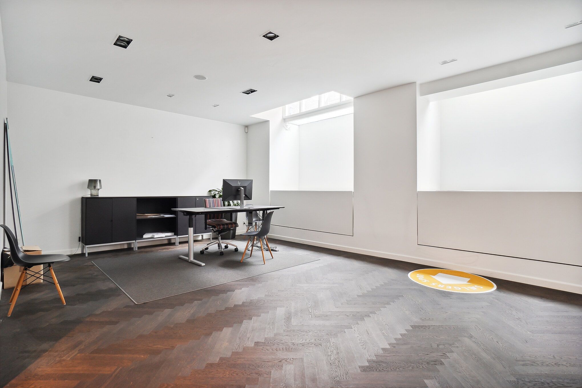 To moderne møbler står i et hvidt kontor med lysegul gulvbelægning og en skrivebordslampe