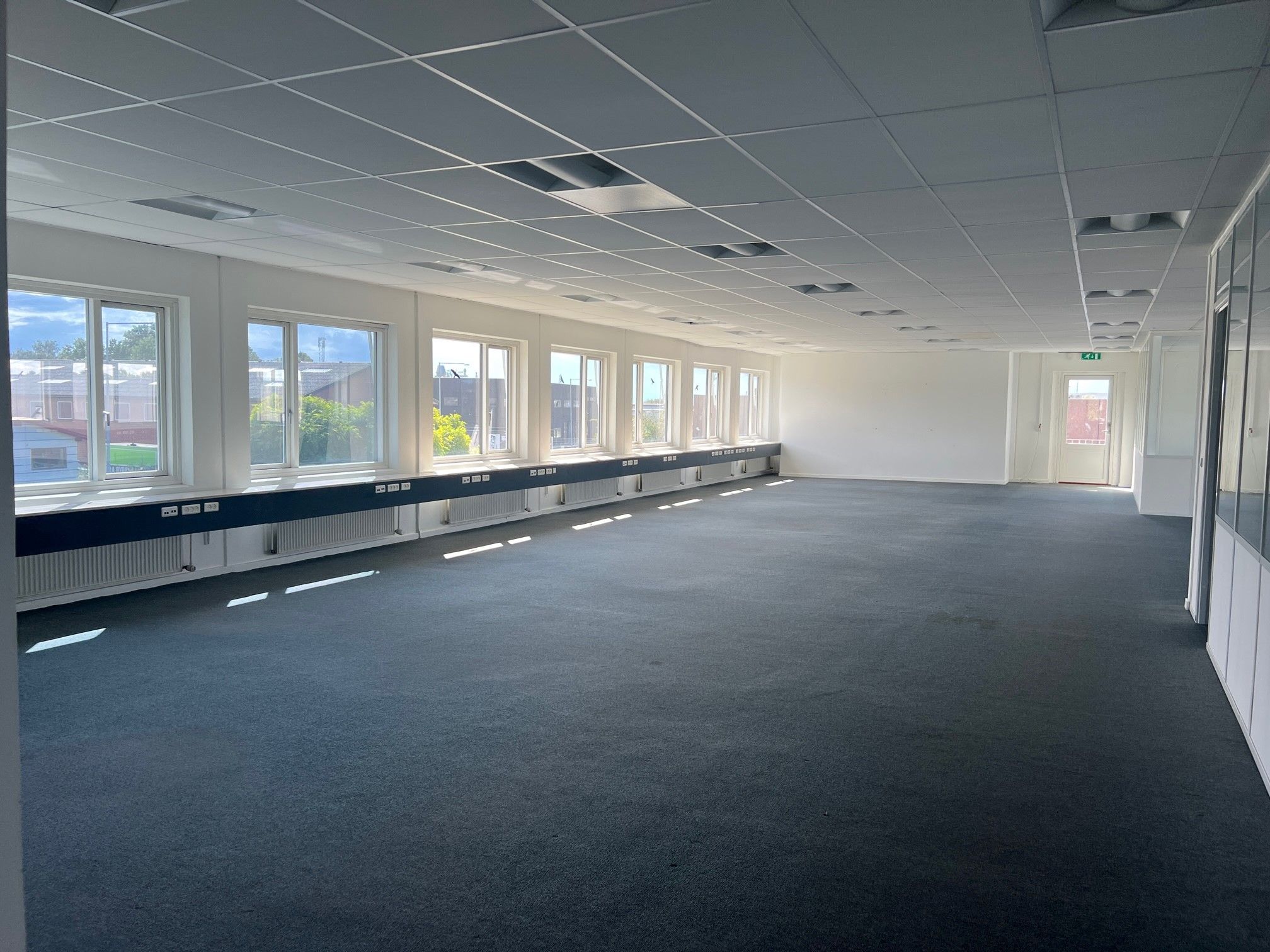 Et stort, lyserødt lokale med store vinduer, gulvbelægning og hvide vægge