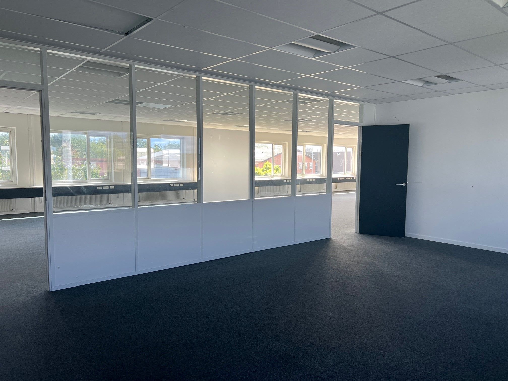 Et stort kontor med lyseruder og et åbent område med en glasdør og en hvid væg