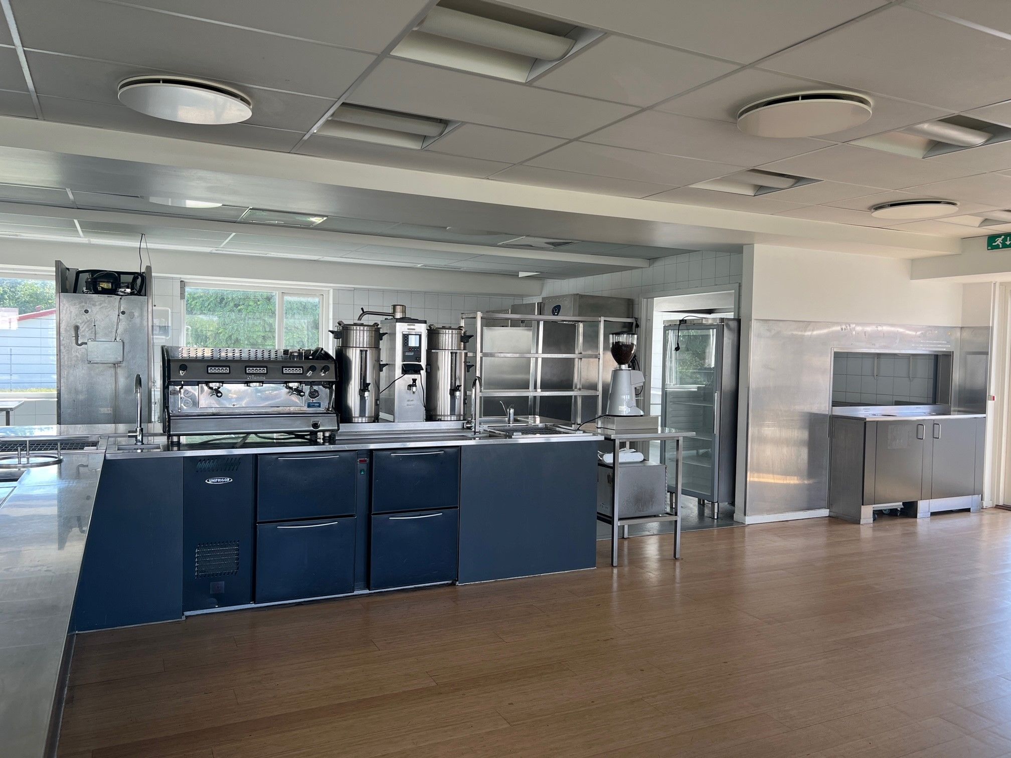 Et kommercielt køkken med store apparater, lyse lofter, og et fint trægulv