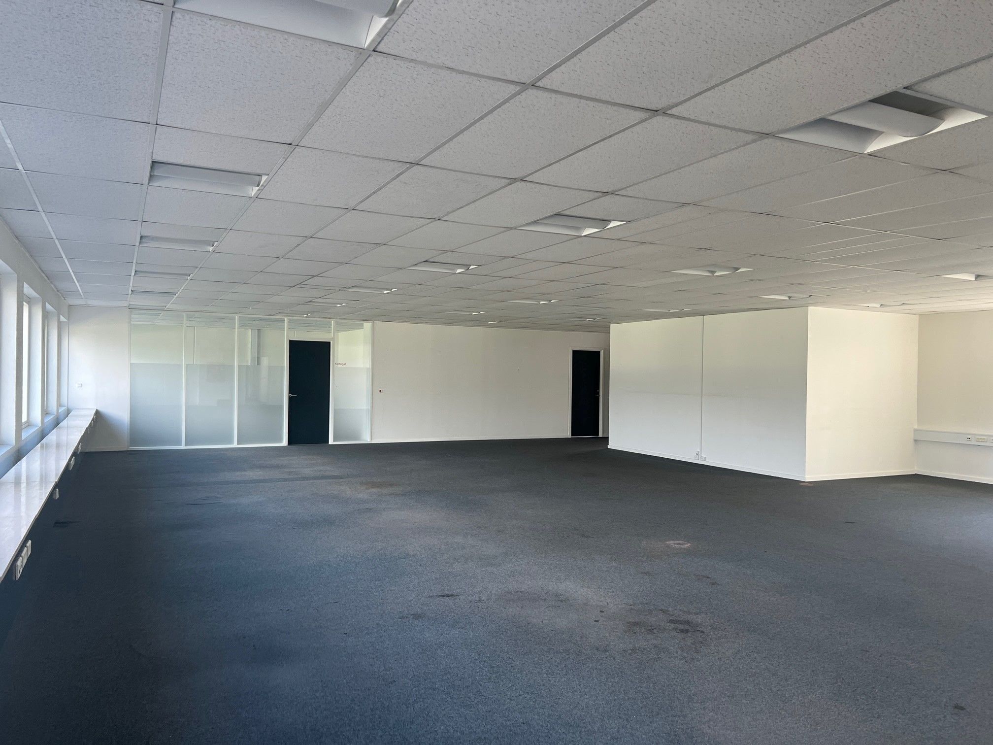 Et stort, ubeboet kontor med hvide vægge, glasdøre og gulvbelægning samt højt til loftet