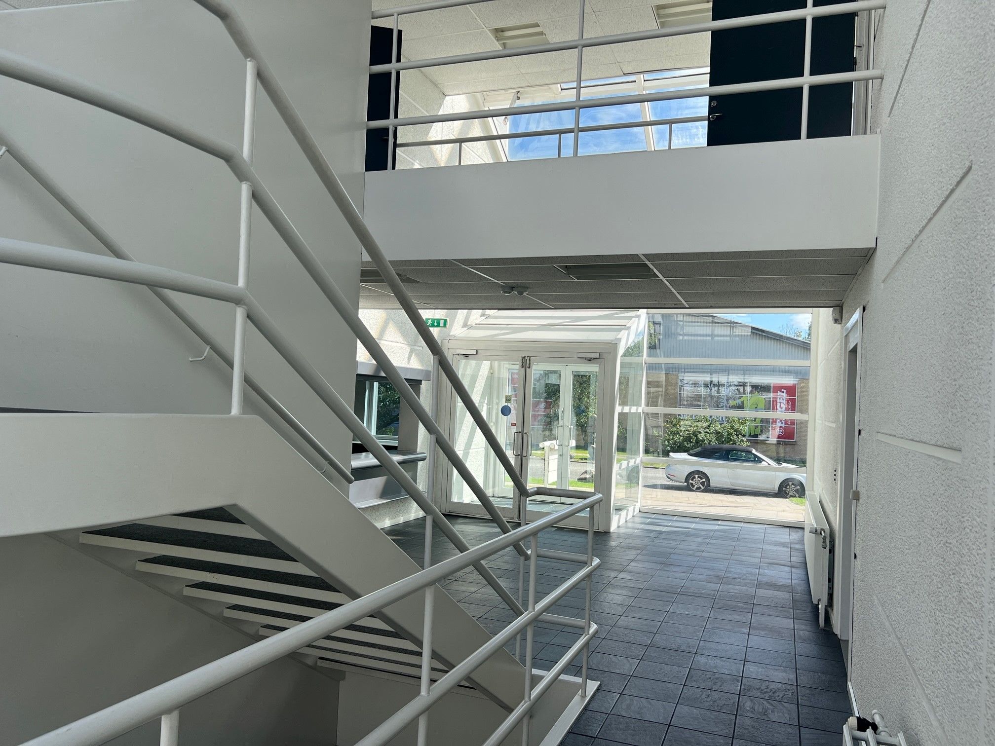 En stor hall med hvide trin og metalgelænder og et stort glasdækket område med en bilparkeringsplads