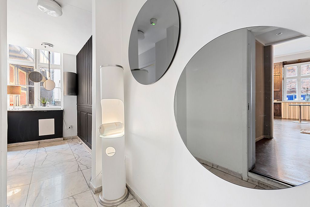 Et minimalistisk og stilrent interiør med hvide vægge, spejle, et gulv i marmor og et toilet med moderne design