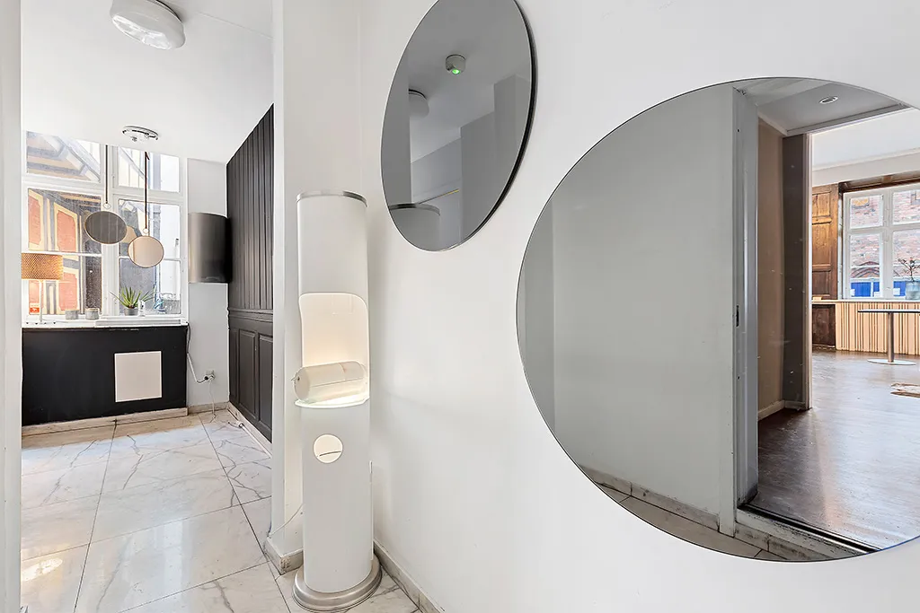 Et minimalistisk og stilrent interiør med hvide vægge, spejle, et gulv i marmor og et toilet med moderne design