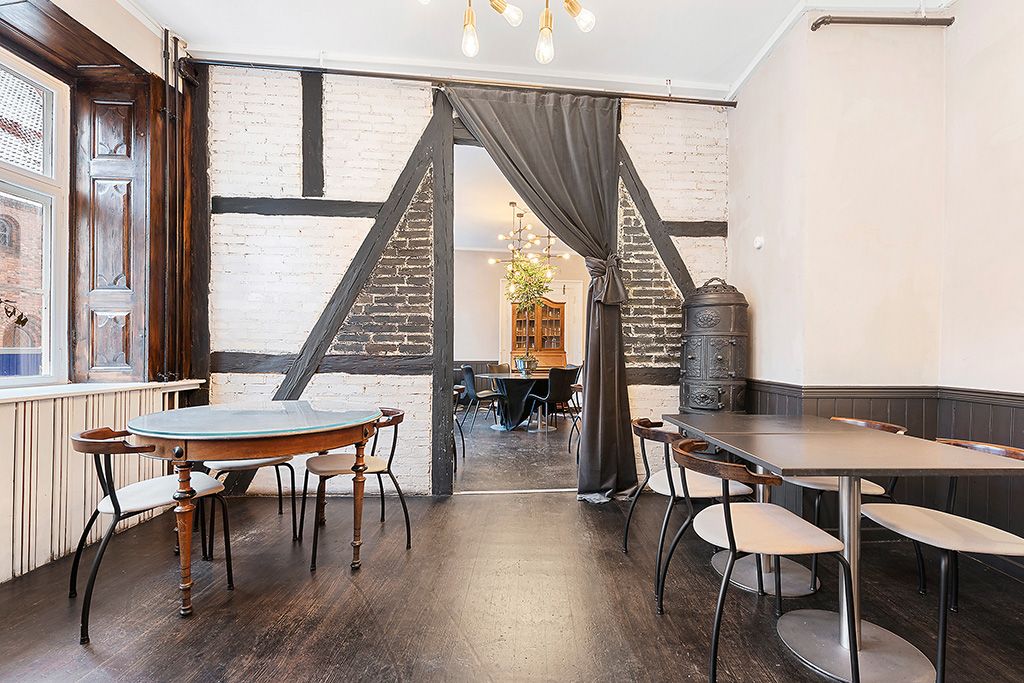 Indvendigt rum med lyse loftslampe, runde og firkantede borde med stole, dekorative bjælker og træpaneler