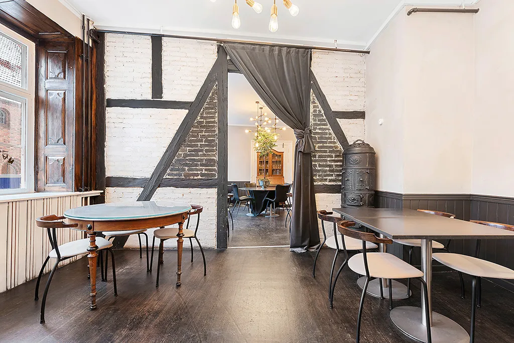 Indvendigt rum med lyse loftslampe, runde og firkantede borde med stole, dekorative bjælker og træpaneler