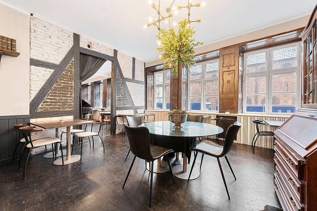 En moderne, glasrunde spisebord og stole samt andre stole og borde i et møbleret lokale med ekspresiv interiør og lyse