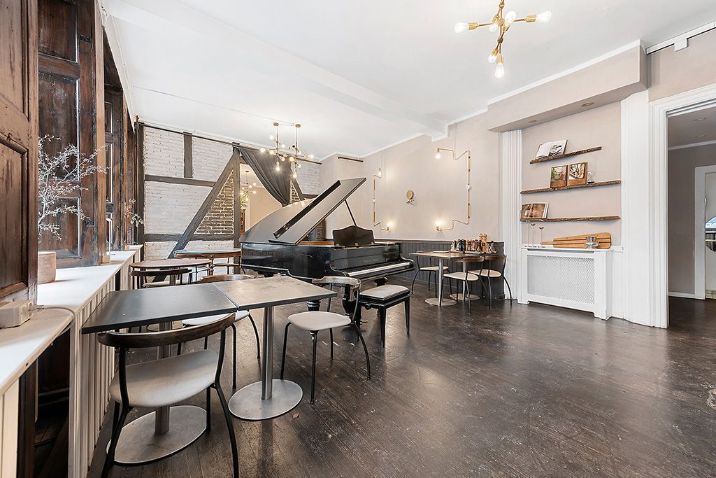 En stor sort klaver i en stilfuld stue med lyse loftsbjælker og hyggelige stole og bord.