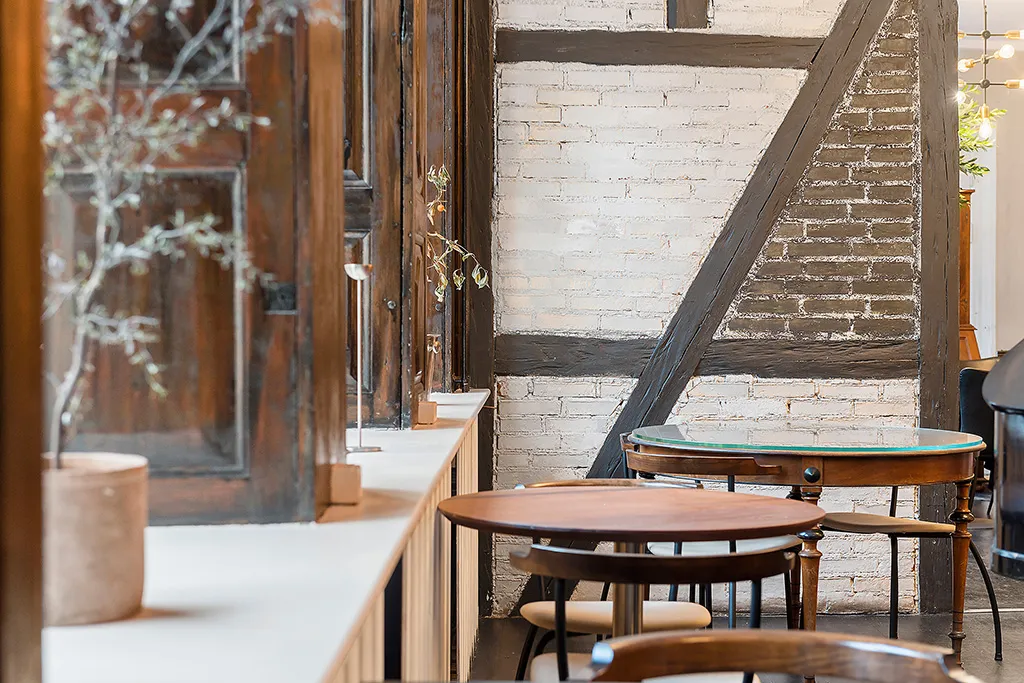 Smukt indrettet restaurant med tre runder borde og høje stole og en hvid mur med træbeslag