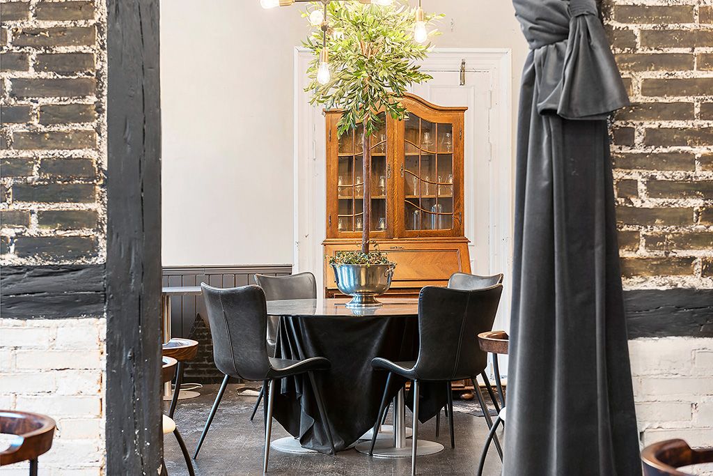 Et elegant bord med sort tekstildækning og læderstole. Lyskrone med flere pærer og et stort plante i en vase