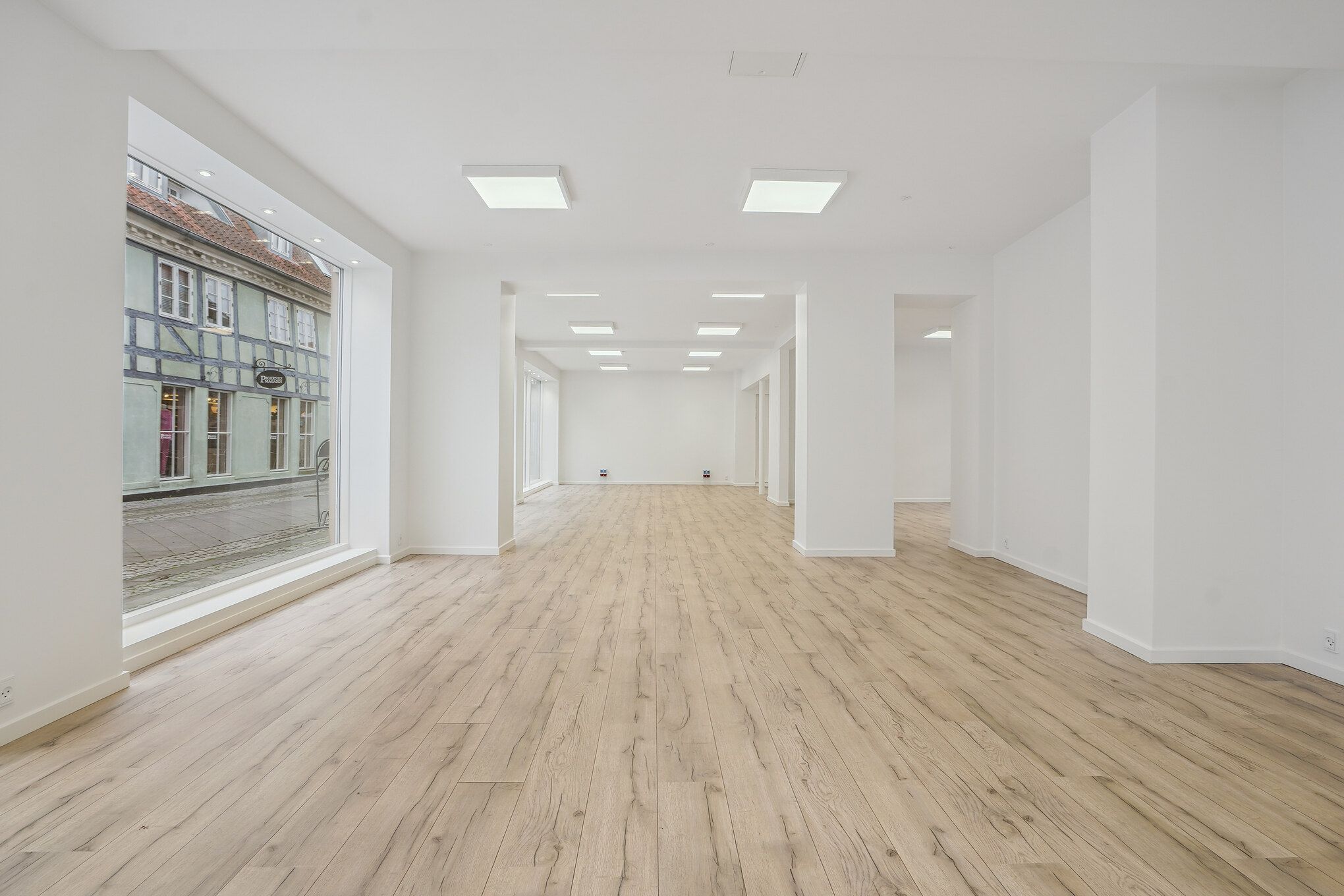 En stor, lyse og moderne butik med hvidt loft og vægge, hårdt trægulv og store vinduer mod en gade med bygninger