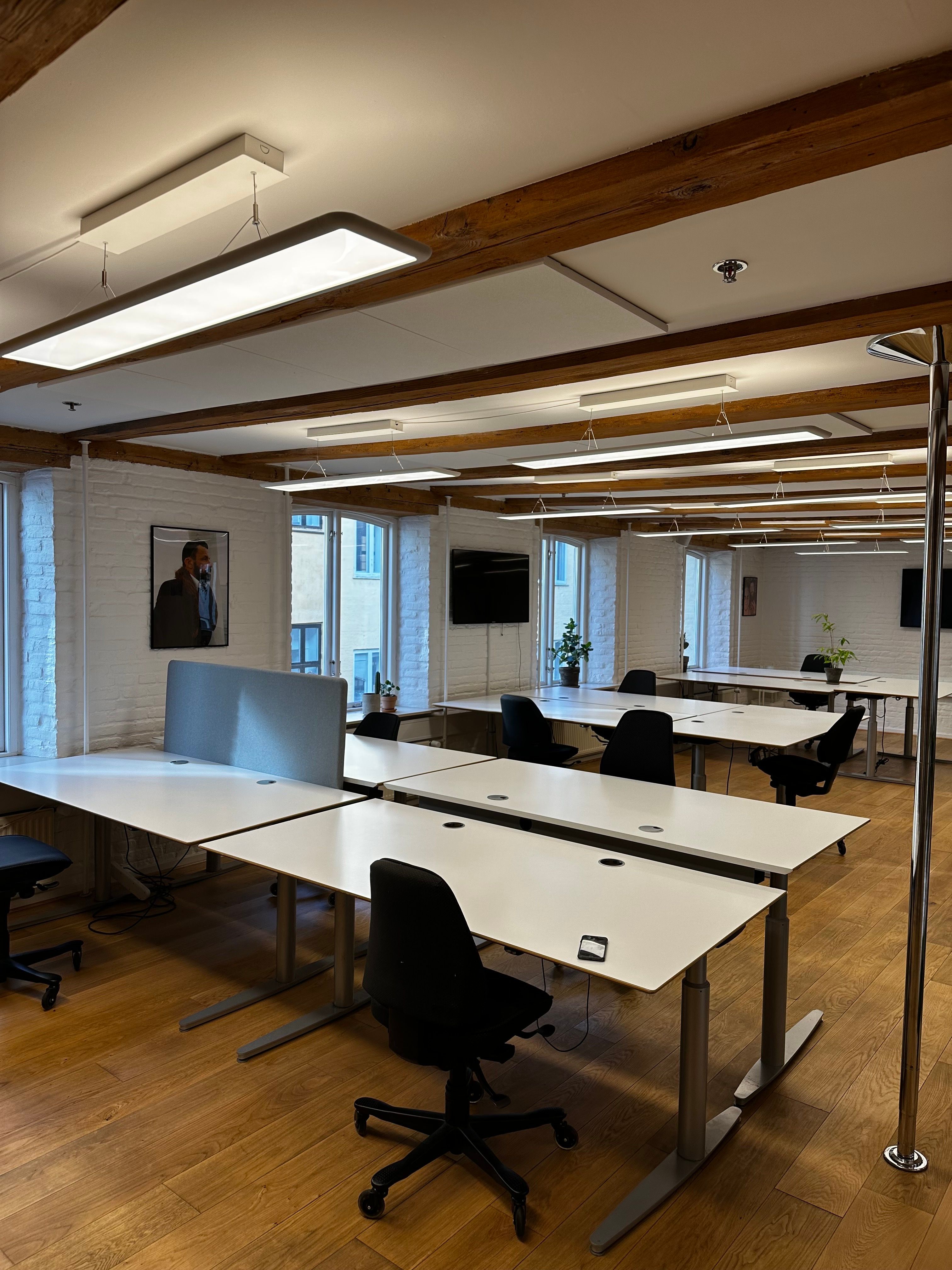 Kontorlokaler med højloft, hvide vægge, træloft og møbler i sort og hvidt og en person på vægbilledet