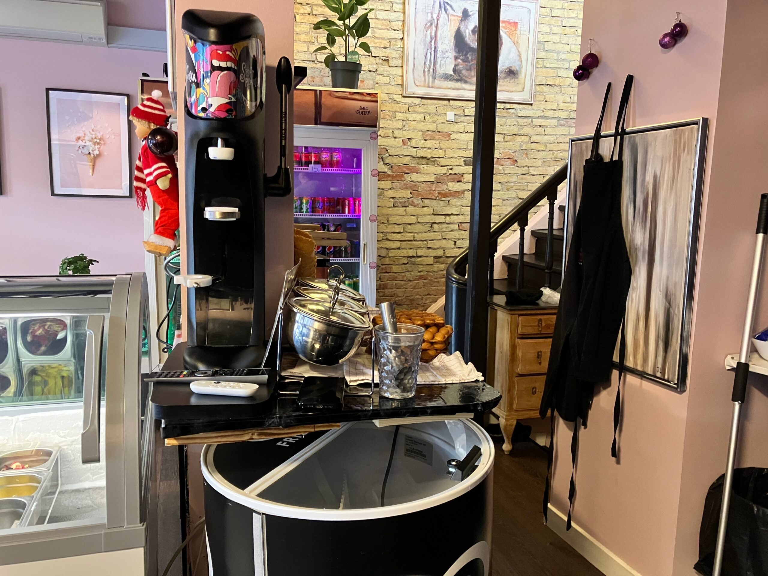 En ismaskine med forskellige smag står ved siden af en skandinavisk isbar i Næstved med lyserøde vægge og lysegul