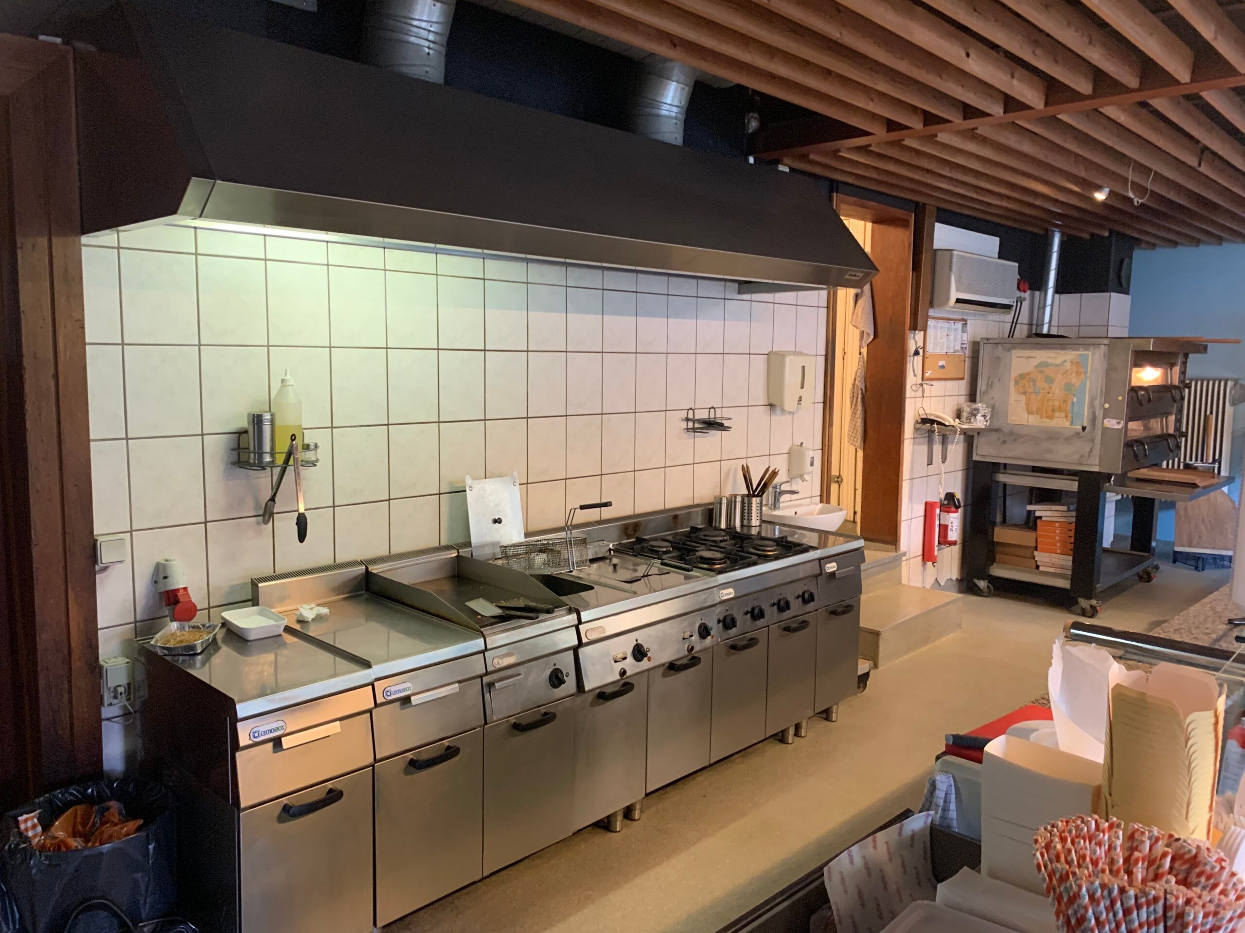 En ren og veludstyret køkken med moderne komfurer og ovne og en stor ventileringsbøjle over for at suge røg og lugt væk