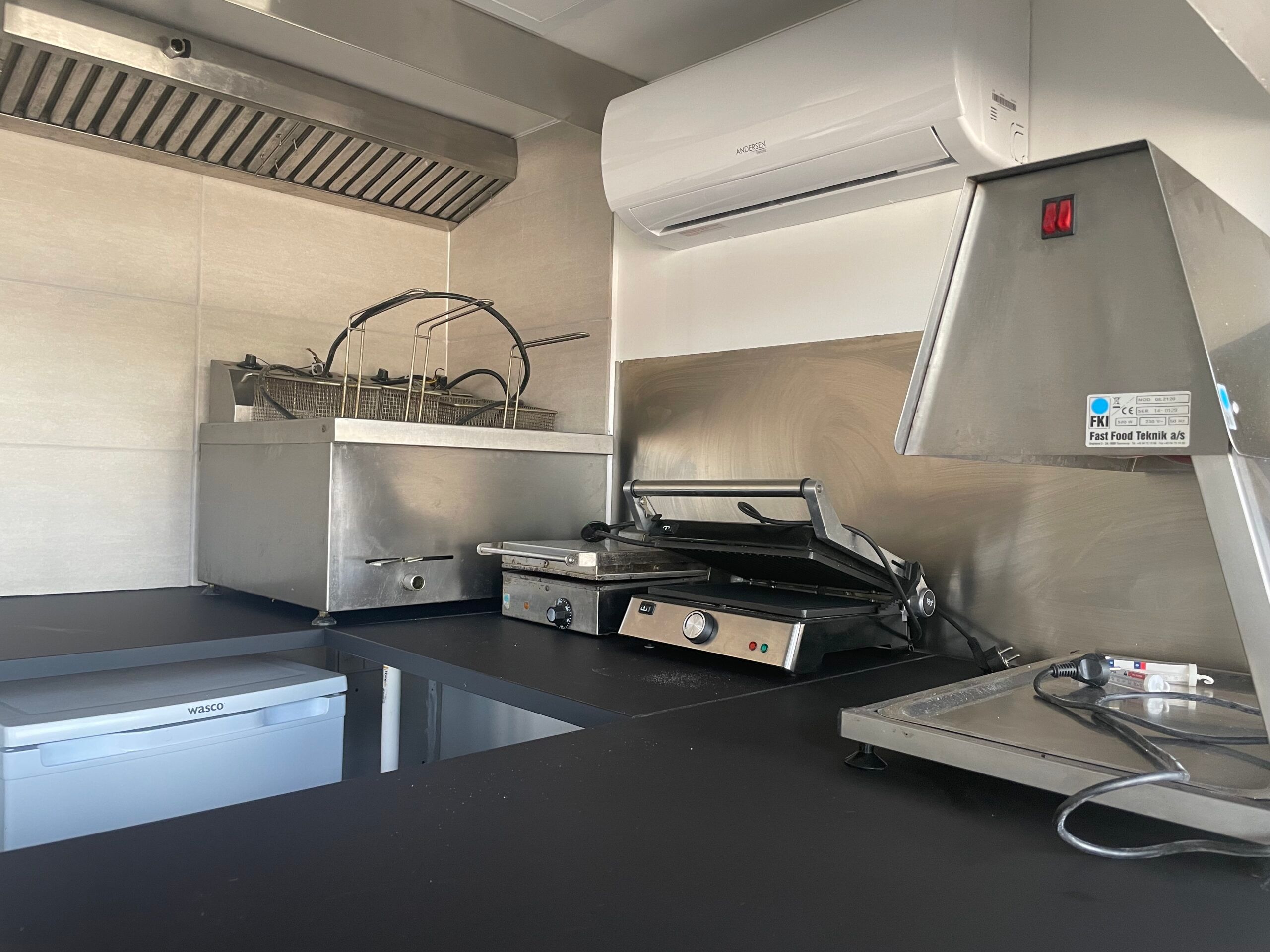 I et renoveret køkken står en grill, en komfur, en fryser og en høj køleskab på gulvet