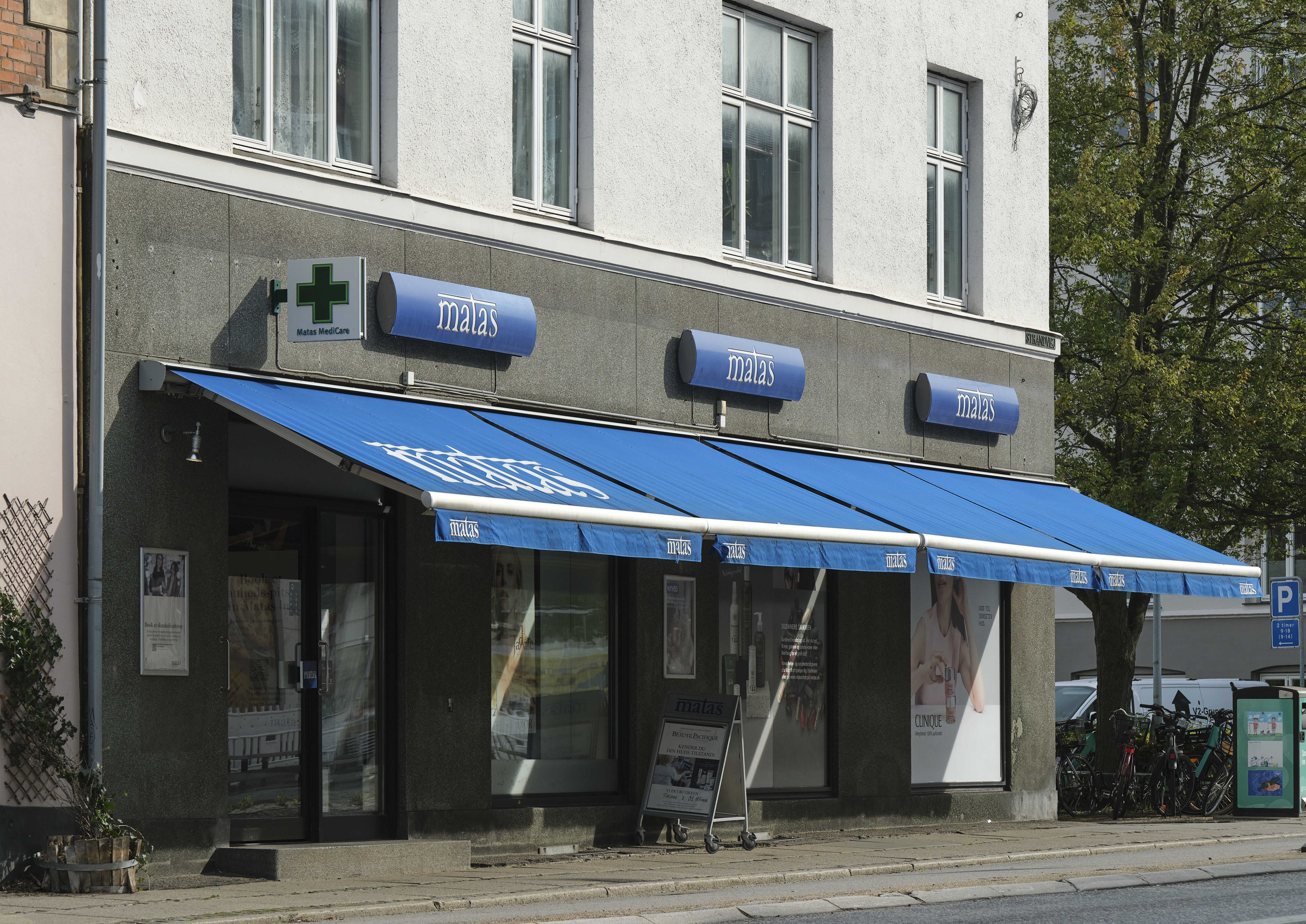 Matas medicinforretning med blå vævet forhæng og hvide bogstaver samt et hvidt kryds i blåt felt med teksten Matas MediCare