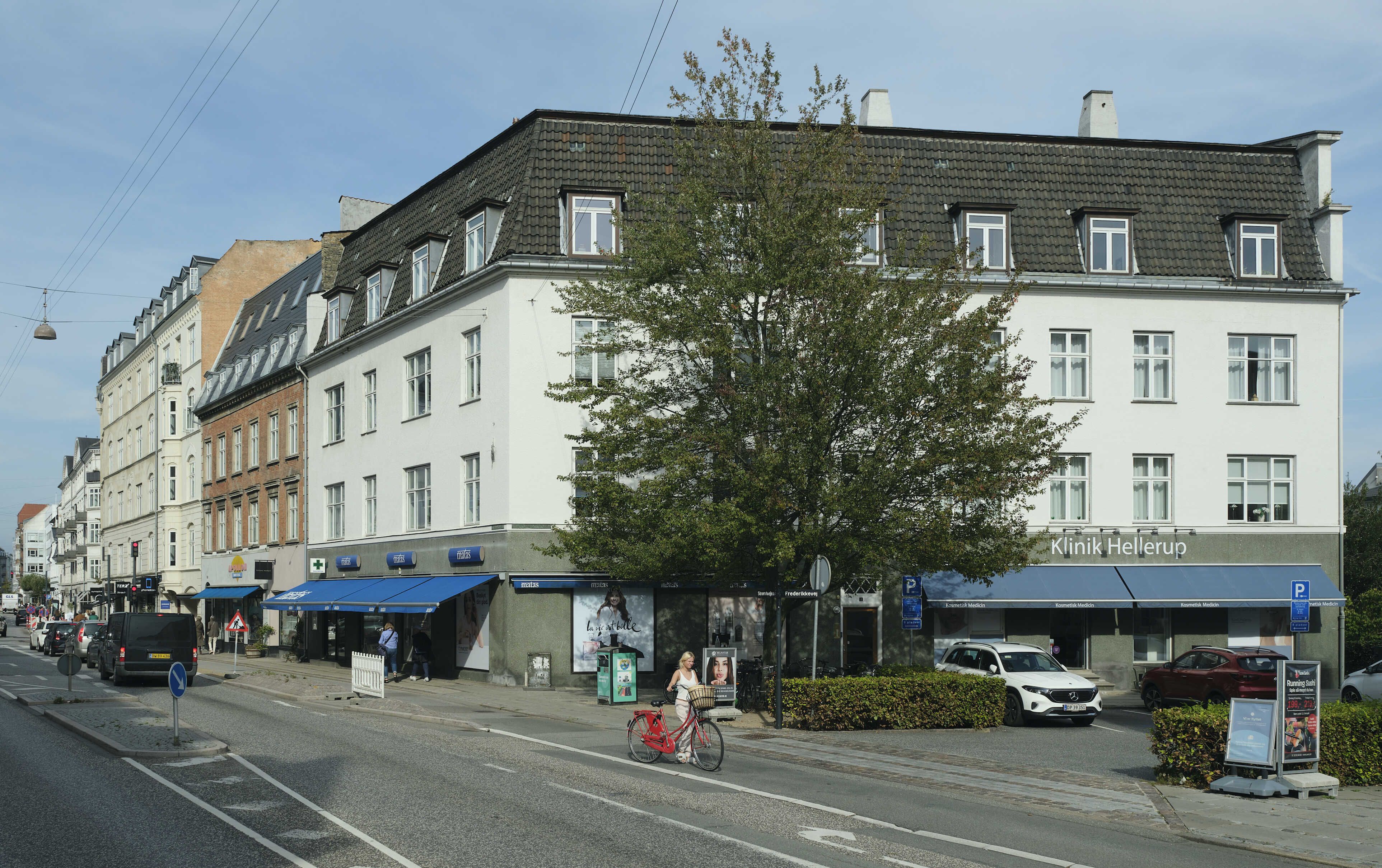 En dame kører på en rød cykel langs Strandvejen i Hellerup med Klinik Hellerup på hjørnet