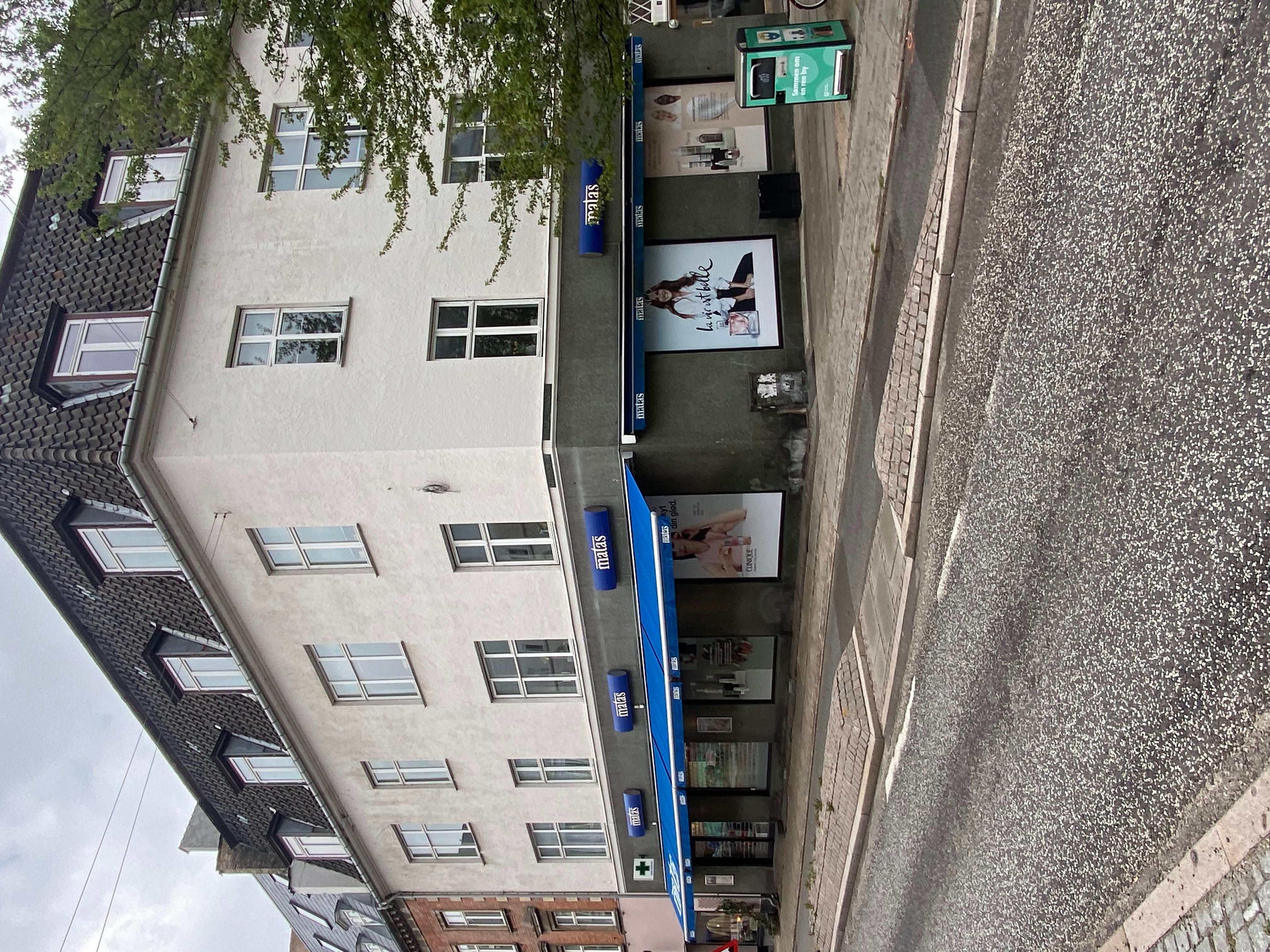 Et højhus med flere lejligheder og butikker på første sal og gadevej, samt salgsskilte på butikkerne og et reklameskilt med