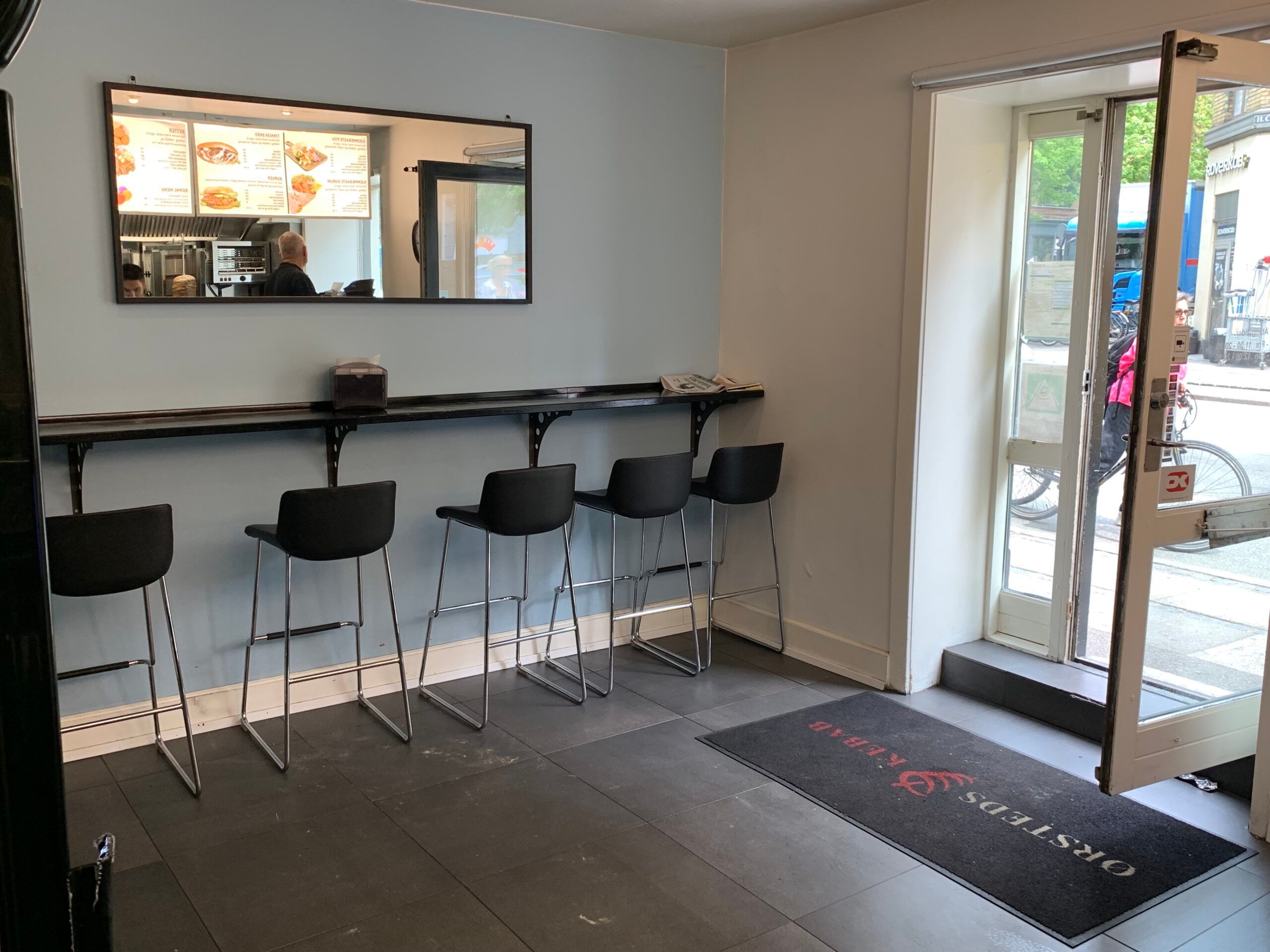 Fremtrædende udsigt til H.C Ørstedsvej 38, Frederiksberg. Sort bar med fem høje stolen. Dør og glasdør står åben.