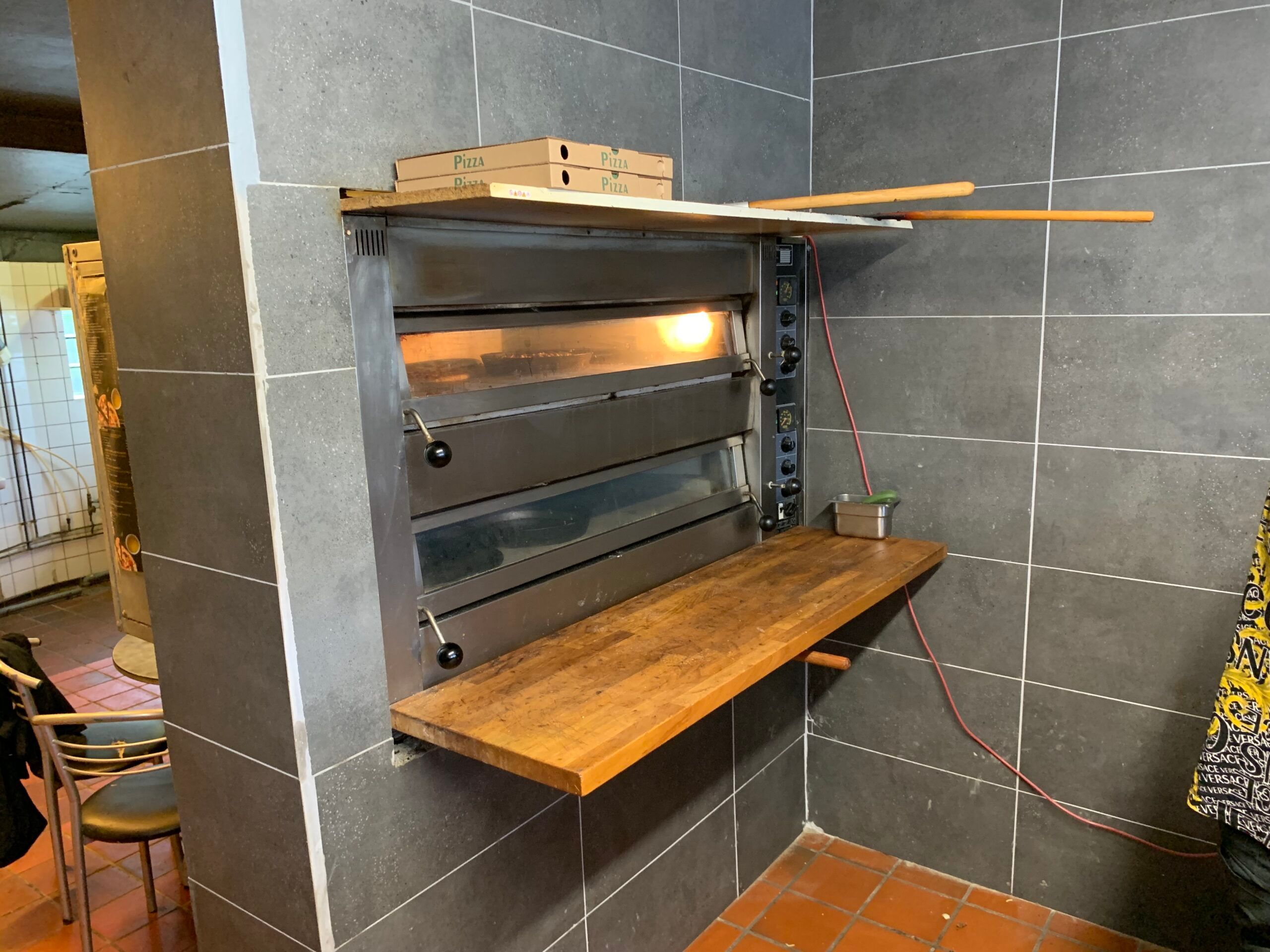 Pizzaovn med træbrætter og trægreb til at skubbe pizza ind og ud af ovnen samt pizzakartoner placeret ovenpå