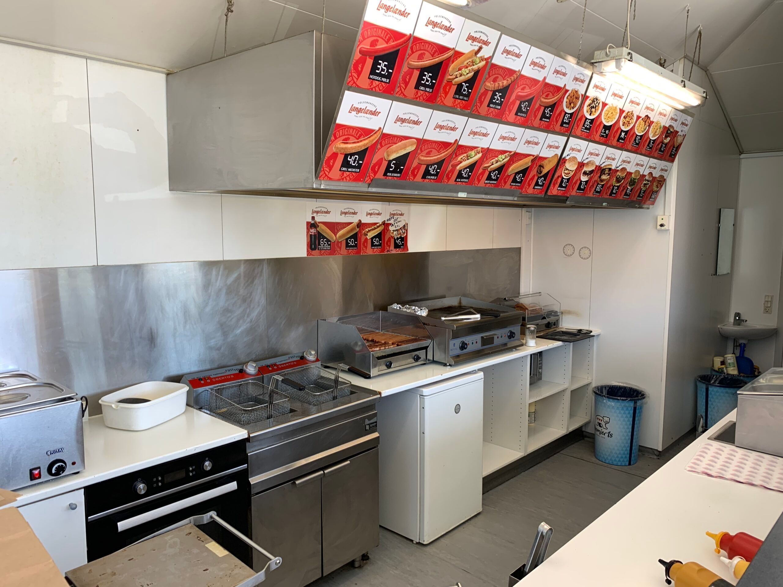 En moderne køkkenrum med højt hængende menukort, en række køkkenapparater, renseri og et skrivebord med ketchup og mayonnaise