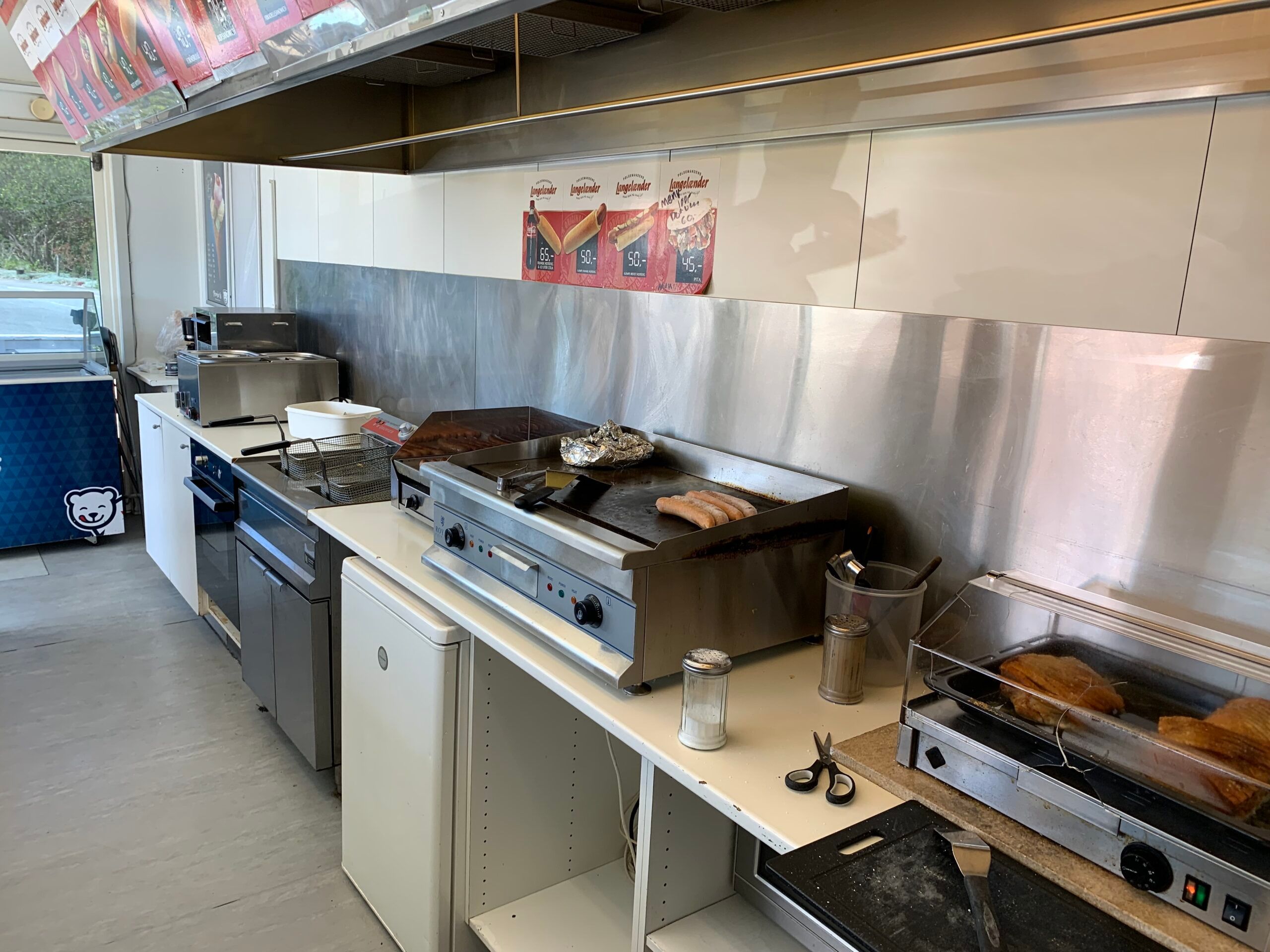 Køkken med grillplade og varmeapparater, røgsuger og en lang reklametavle med Longblender-produkter og deres ingredienser