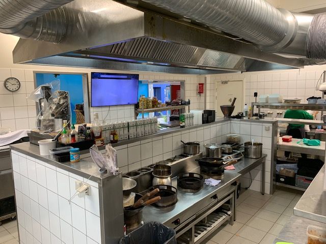 En stor kommerciel køkken med mange apparater, gryder og gryder. Der er en person i en grøn skjorte, der går rundt i