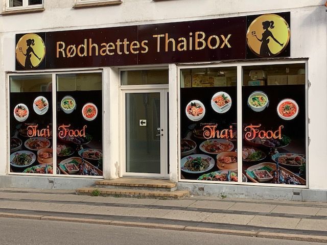 Rødhætte Thaibox er en forretning med thailandsk mad. Logoet viser en kvinde med en rød lue og en Thai-skål. De sælger