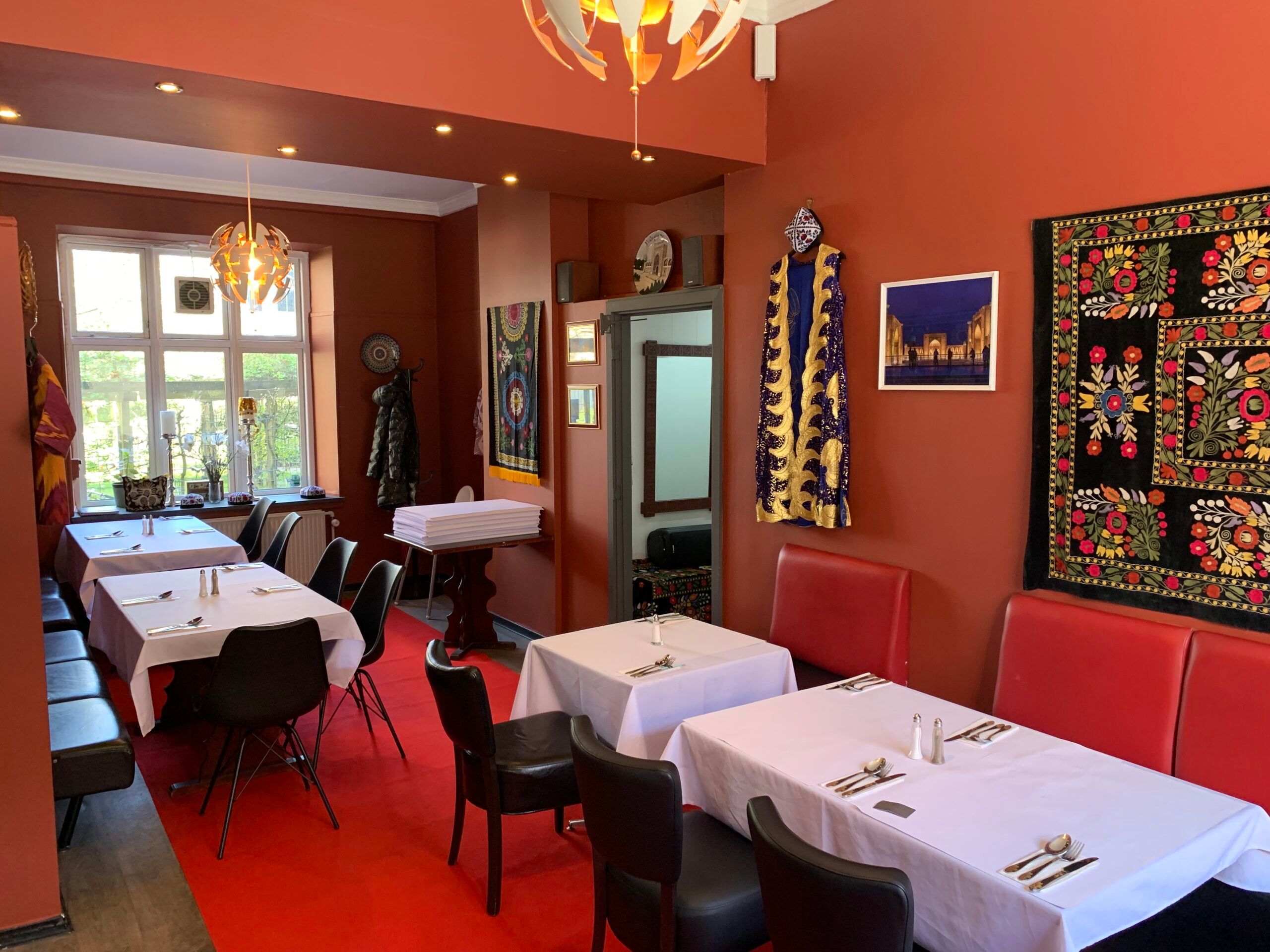 En indretning af en lille restaurant med røde lædersæde og to lange borde med hvide klud og servietter.