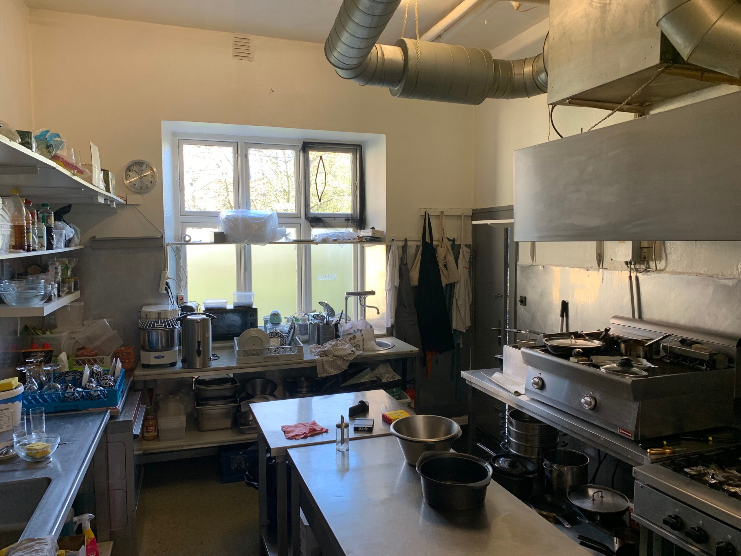 Restaurant med vinduer og køkkenudstyr, små gryder og kogende vand, apparater og flasker, og et ure på væggen