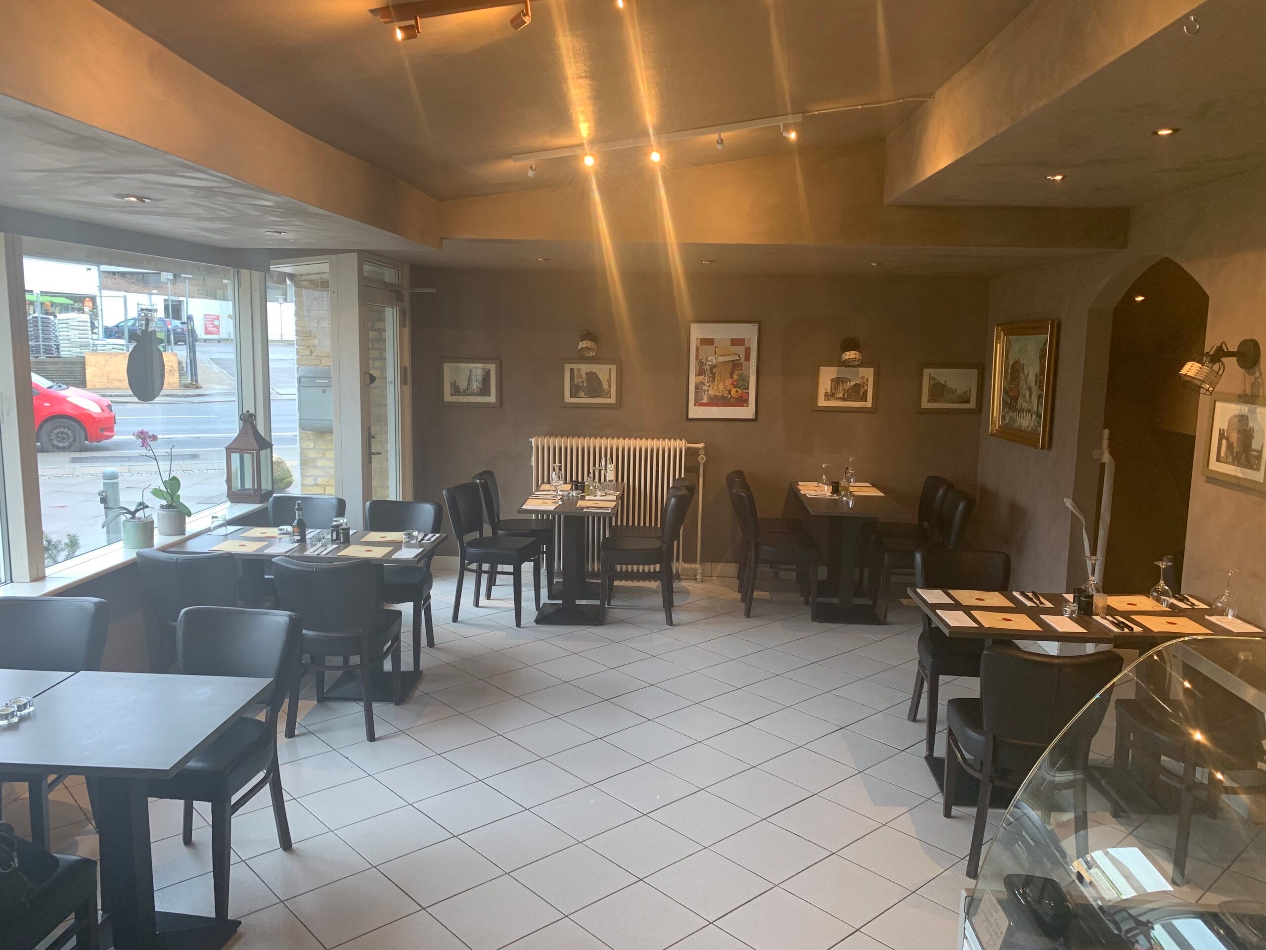 Interiør med borde og stole, hvor der er lyse gulve, vægmalerier og et glas vinglas på bordene