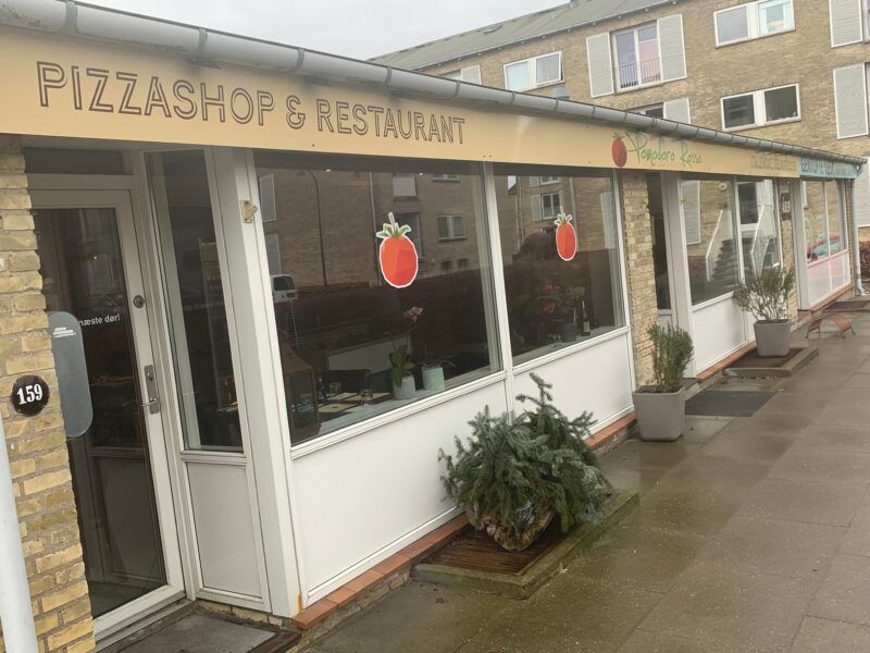 Pizzashop og restaurant med skilte med tomatmotiver og nummer 159. På facaden er der tre store blomsterkrukker.