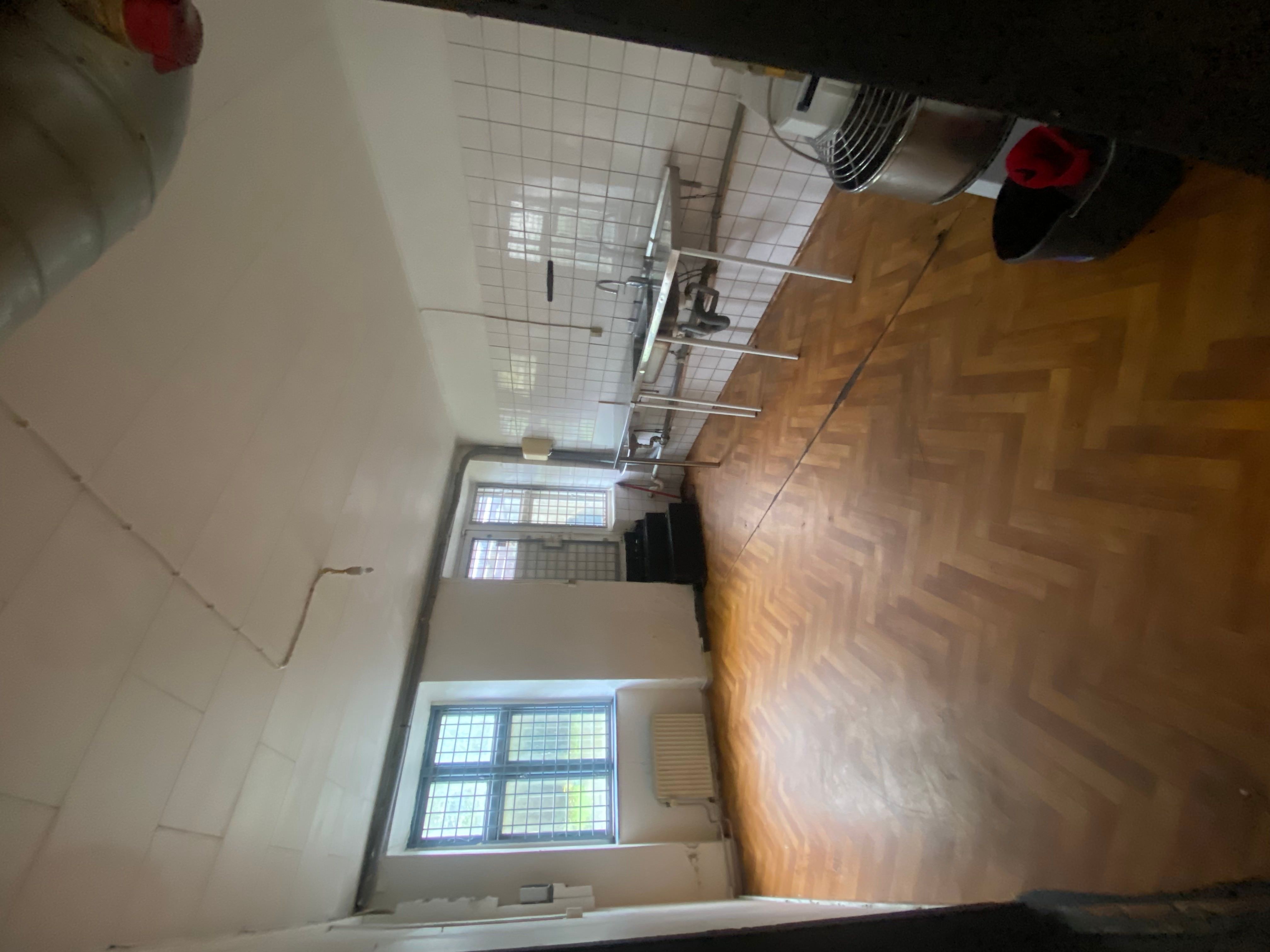 En tom køkkenrum med lyse, hvide vægge og et gulv med en hærdet træfinish. Et køkkenbord med en metaloverflade og en