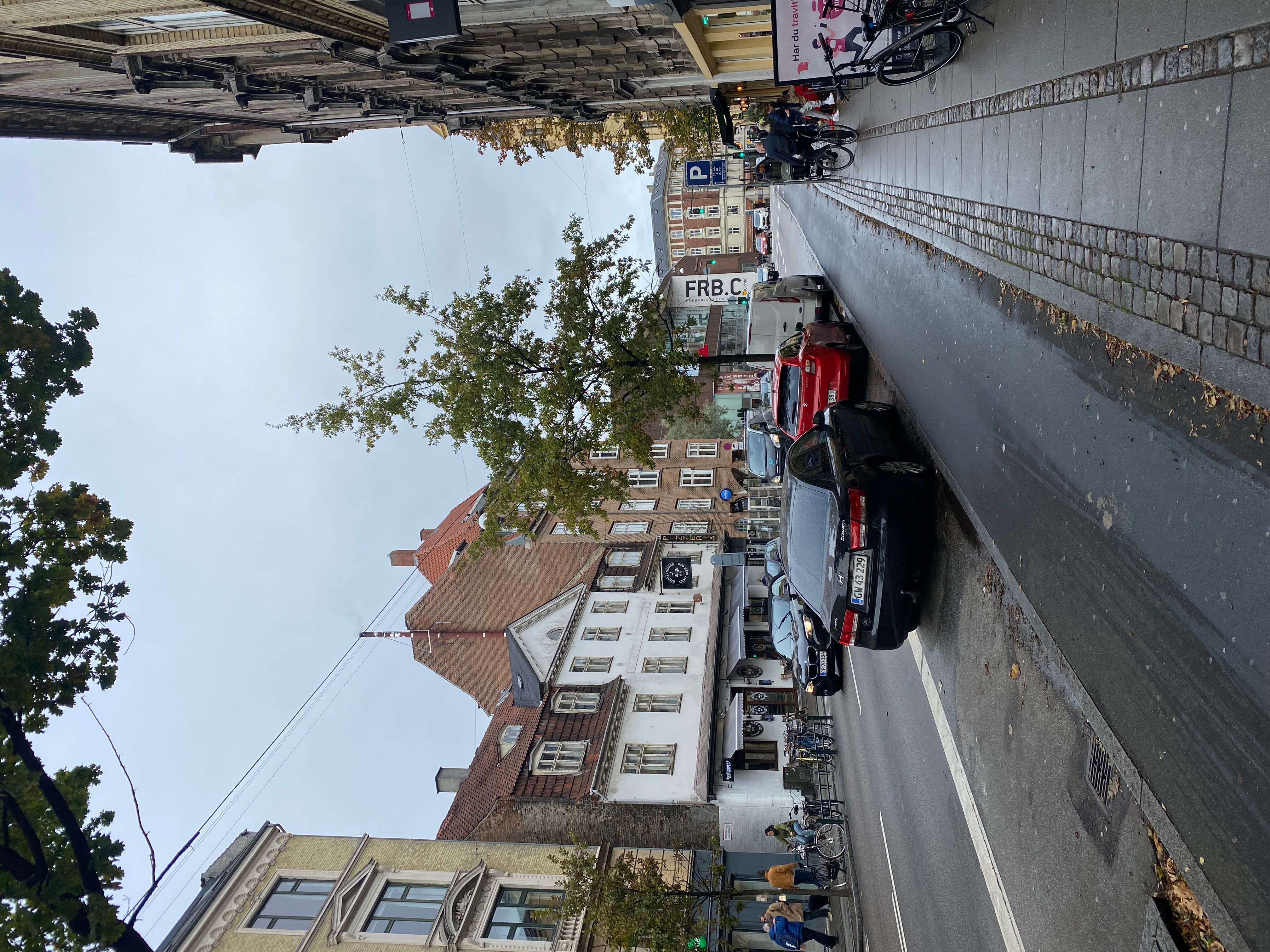 En række parkerede biler, hvoraf den nærmeste er en sort bil, og en række bygninger, hvoraf den nærmeste er en gul bygning