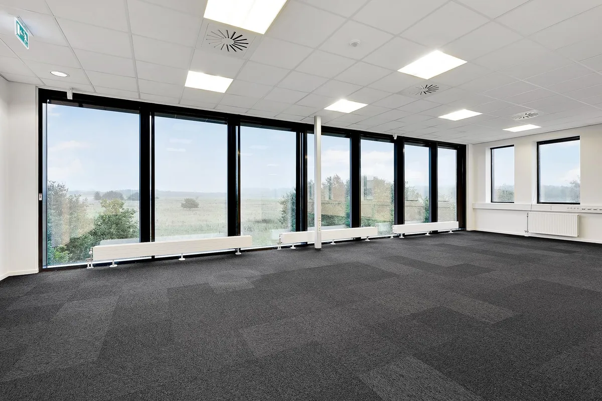 Et moderne kontor med åbent design og store vinduer, hvor sollys strømmer ind og reflekteres af den høje loftsprofil og de