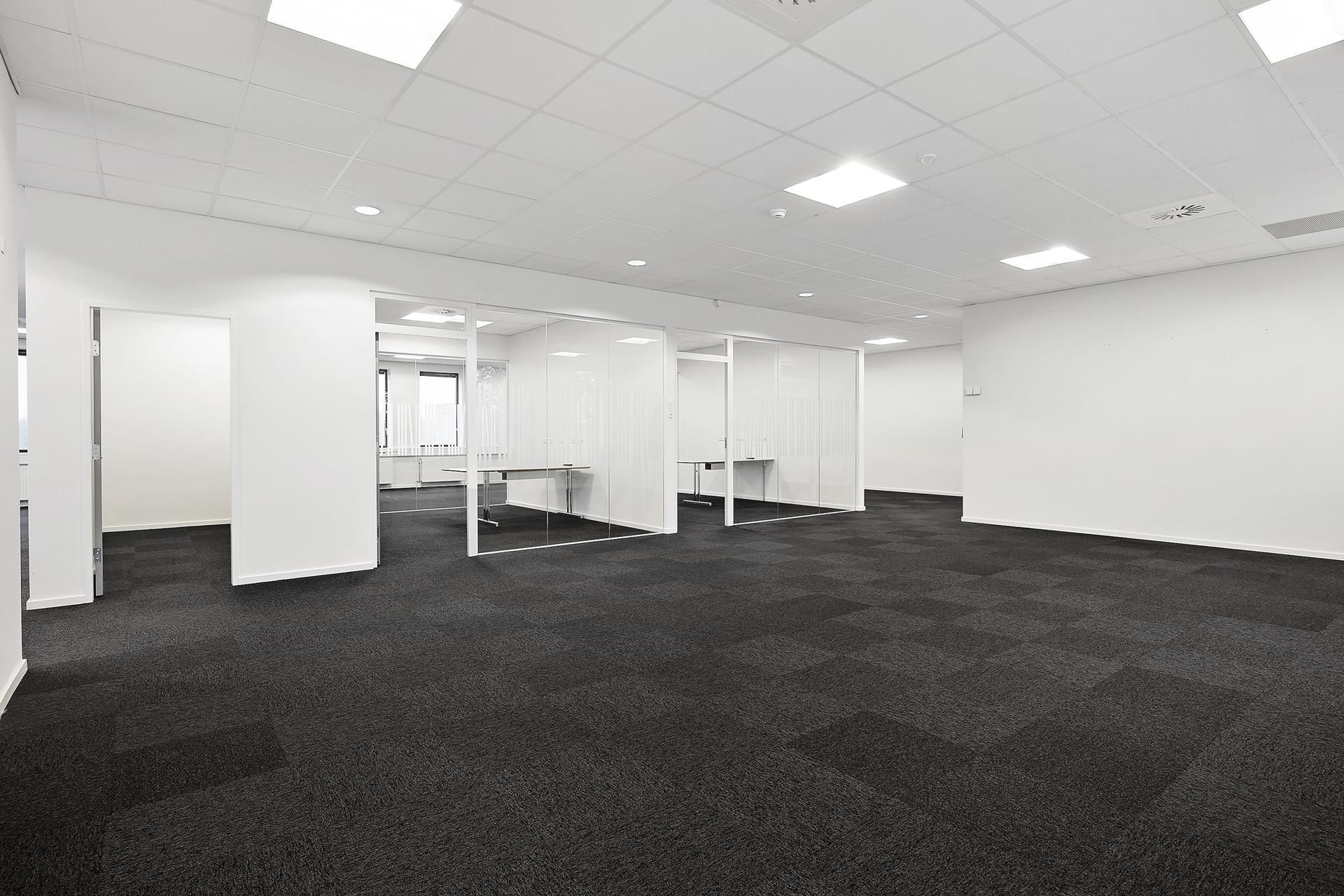 Et moderne kontor med hvide vægge, glaspartier og møbler samt lyse gulvbelægning og højt til loftet med hvide loftsplader