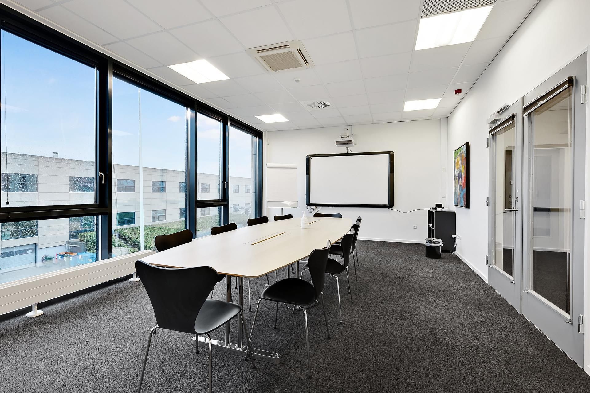 Mødelokale med lyse vinduer og lysegul bordplade med moderne stolpe stående stol med spidse ryglæner, projektionsskærm og