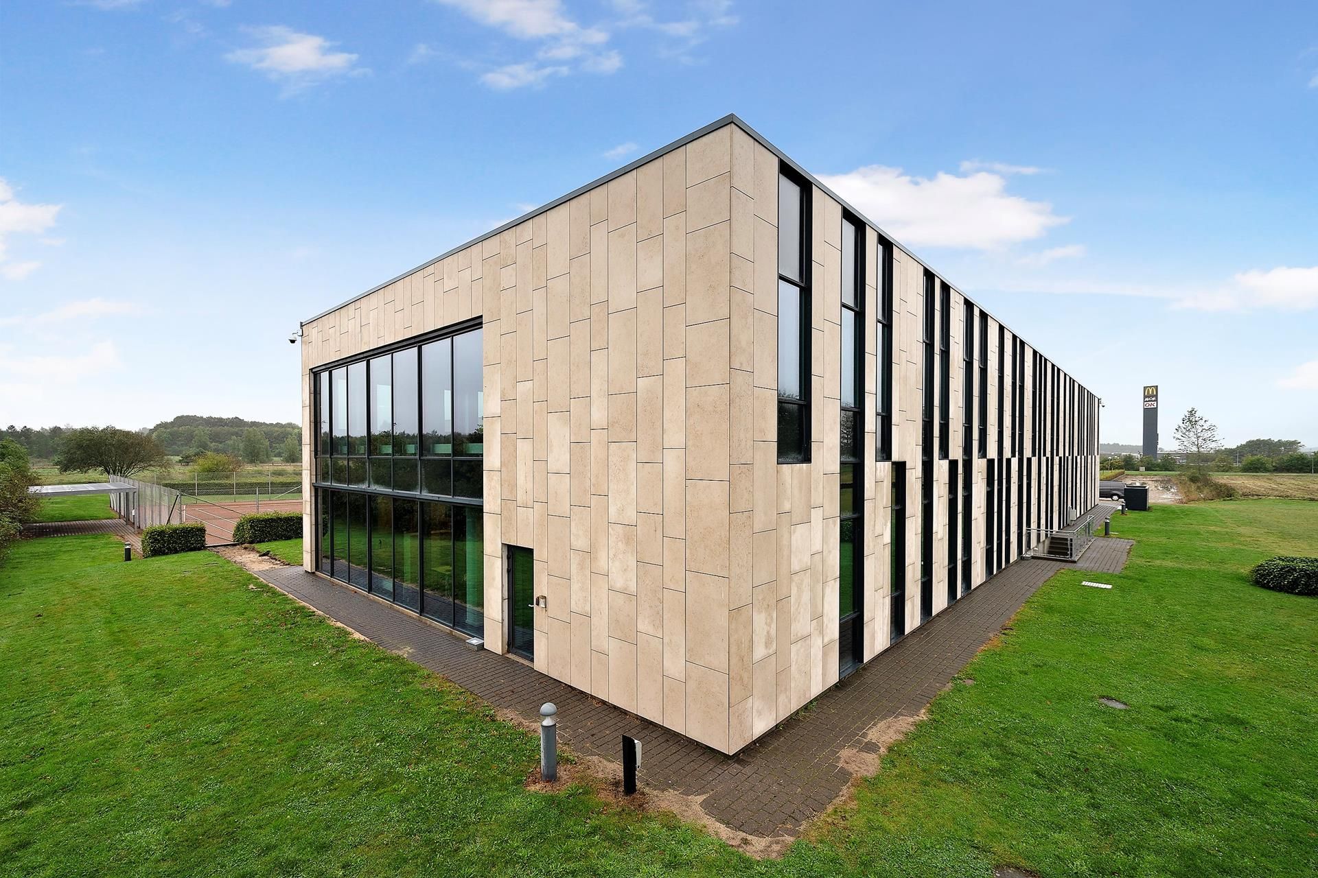 En kontorbygning med gul og beige stenbeklædning, store vinduer og en skravet tagkant. En McDonald's-reklameskilt er synlig