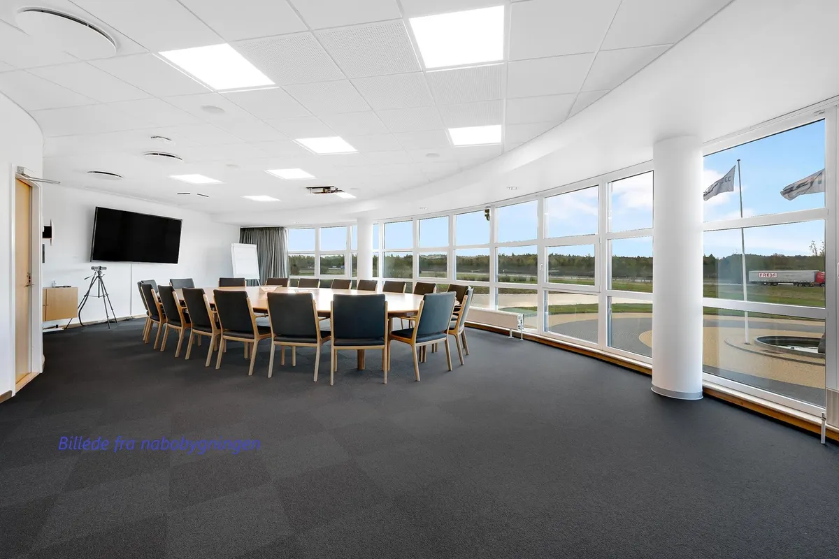 Konferencelokale med runde bord og stole, samt store ruder med udsigt til vej og bygninger