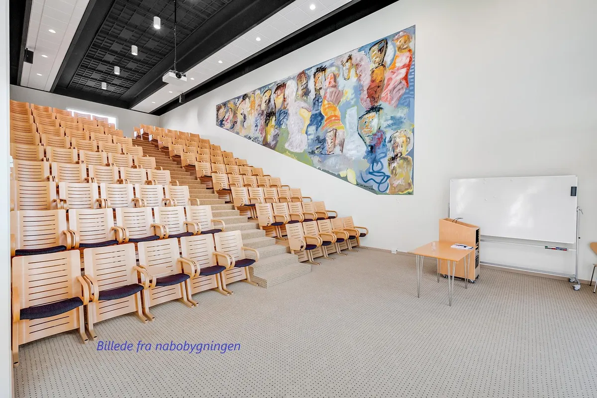 Auditorie med lyse møbler og stor vægmaleri af mennesker og en stor hvidtavle i lokalet
