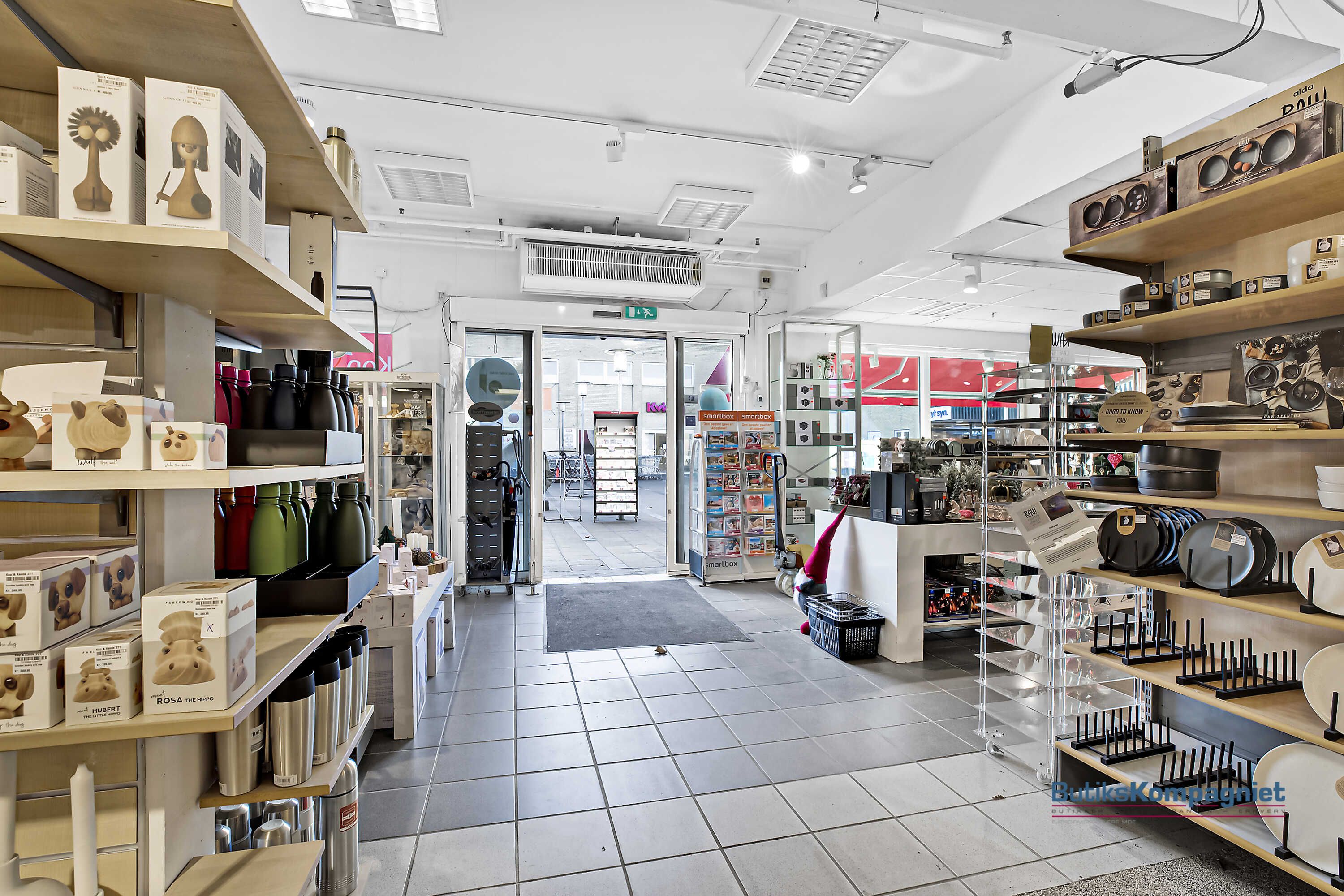 Her er en butik med lyse lofter, hvor der er flere hylder med forskellige produkter som flasker, tallerkener og smykker. Der