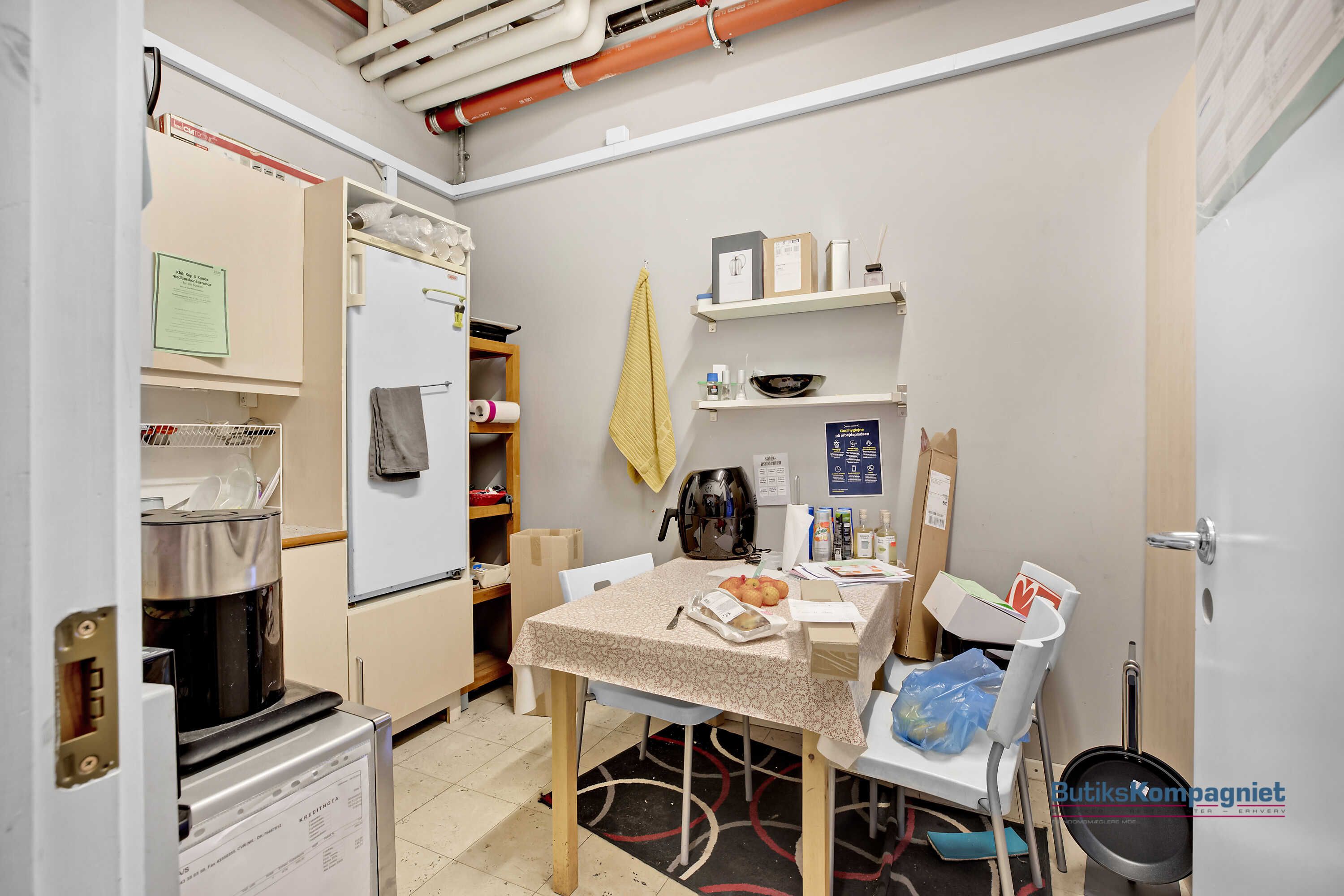 Køkken med køleskab, kogeapparat, bordet med mad og en hængende guldhandsker samt to stole ved siden af det.