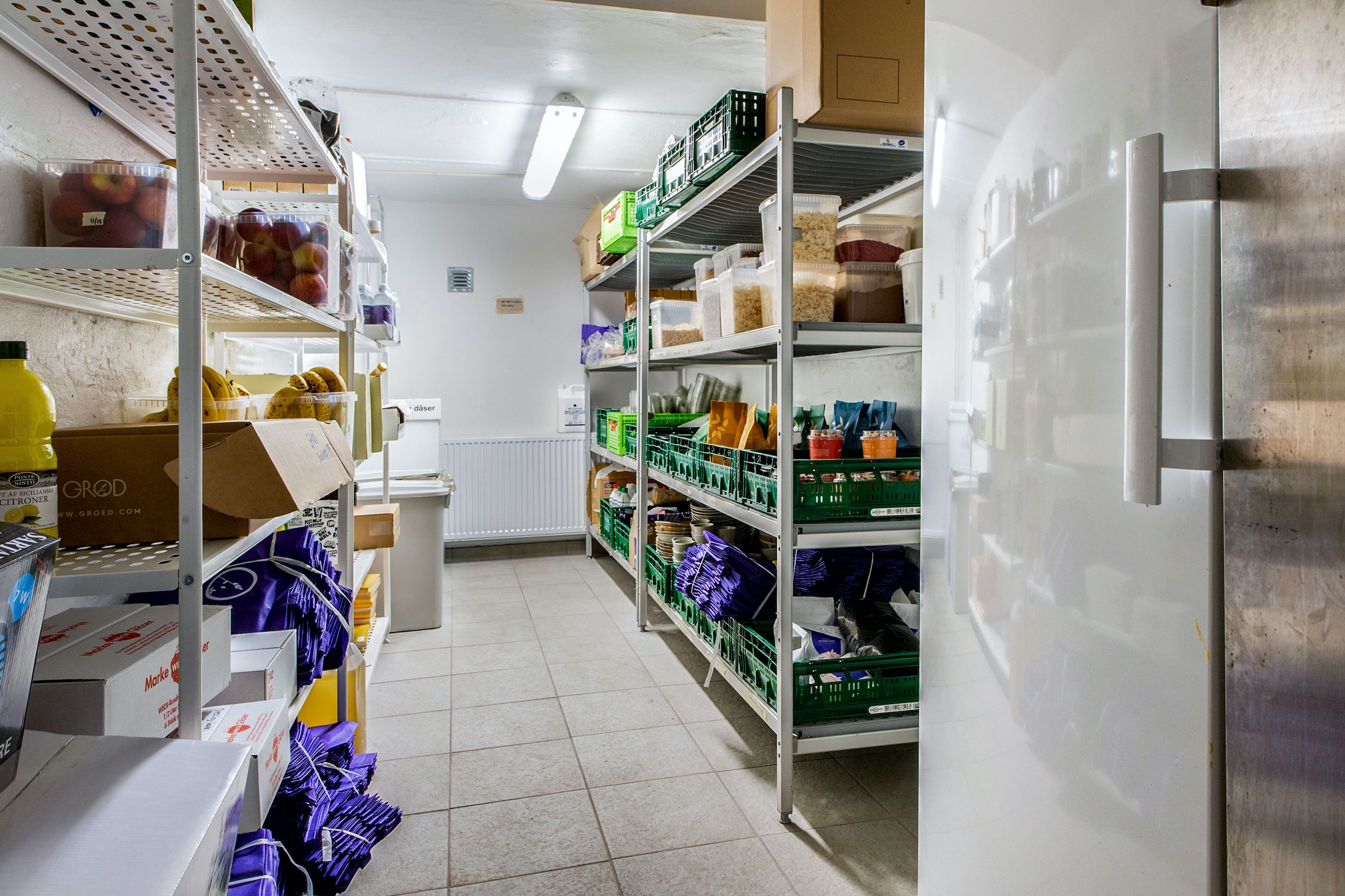 Lager med frugt, grøntsager og andre varer, plastikposer, kartoner og bøsser med varer samt køleskab