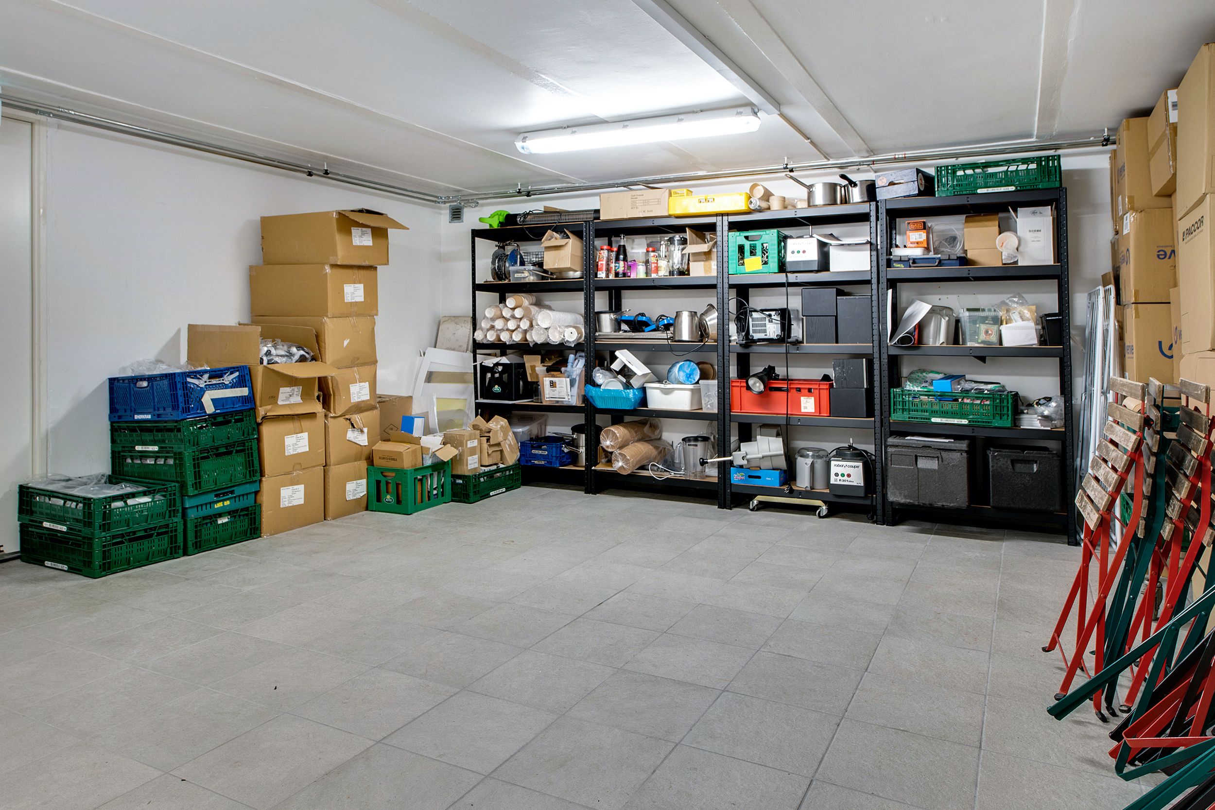 Lager med kasser og hylder, hvor hylderne er fyldt med diverse ting, og gulvet er dækket af fliser