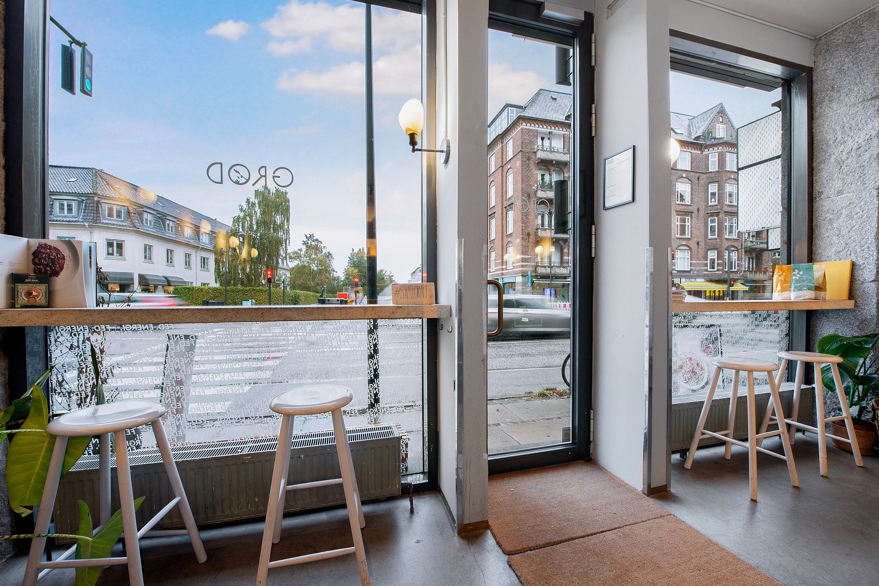 I en hyggeligt indrettet cafe er der høje stolpe og hvide stole samt et trægulv og hvide vægge