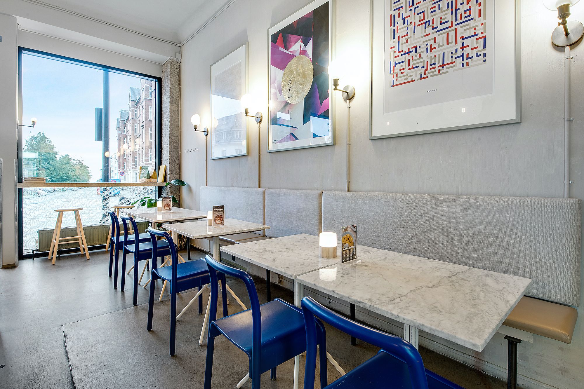 En luksuriøs restaurant med marmorborde, blå stole og vægkunst, og en stor glasdør med udsigt til gadebilledet og bygninger.