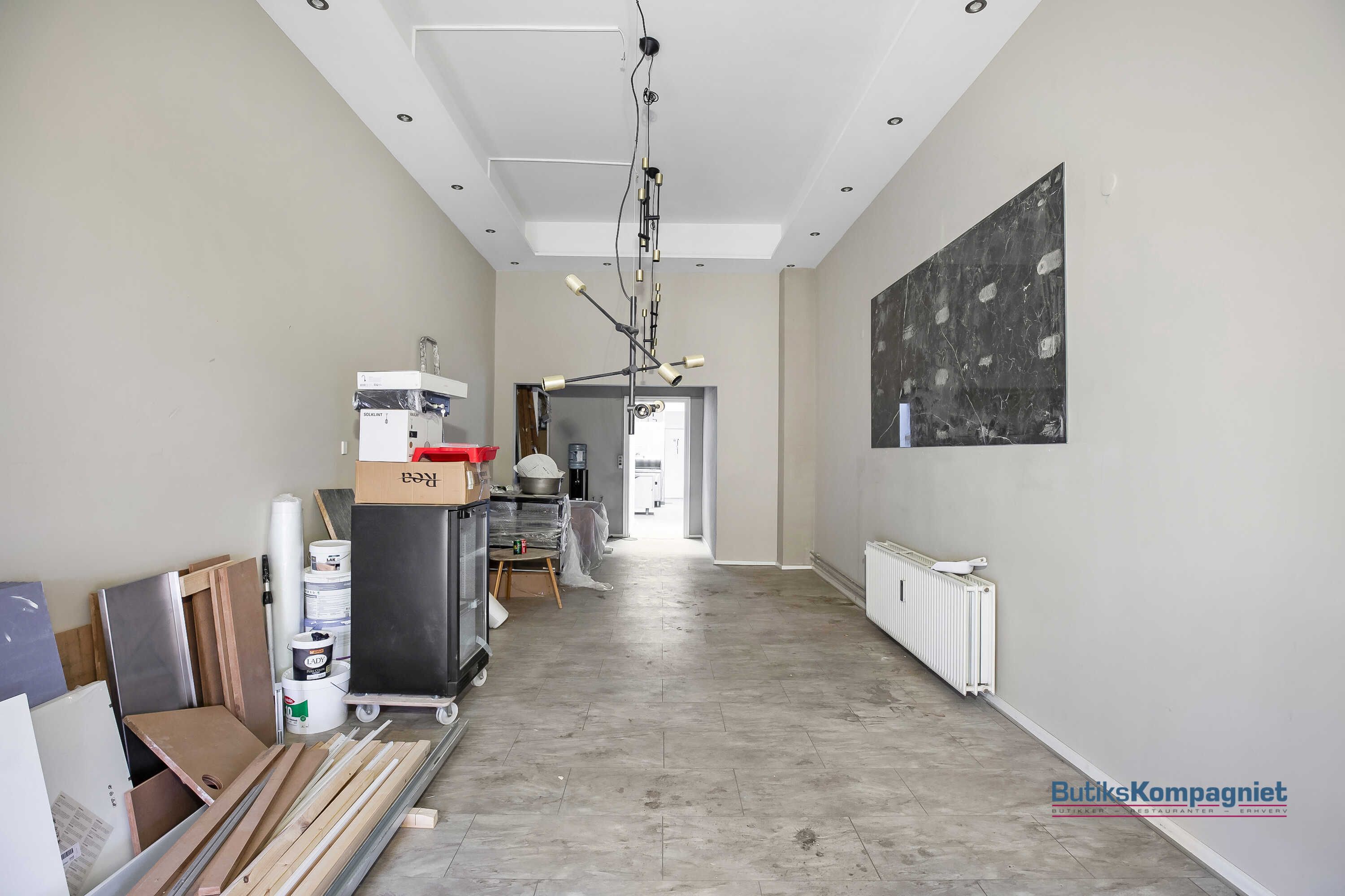 Hallen med højt til loftet, store vinduer og lyse loftslampe. Væggene er hvide og gulvet er lysegrå.