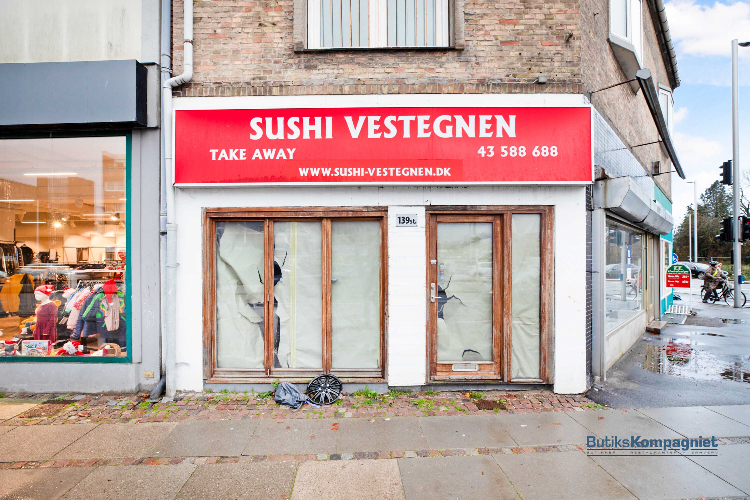 Takeaway-lokaler Sushi Vestegnen i Glostrup med sønderskudt vinduer og sønderskudt dør, hvor en person cykler forbi