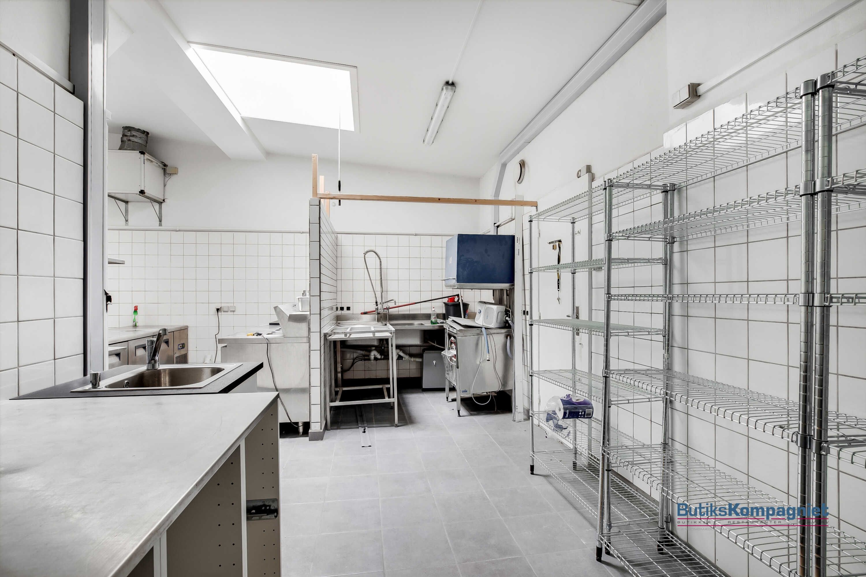 En rummelig og ren takeaway-køkken med flere apparater og udstyr, der er installeret på en metalreol og en metalbord